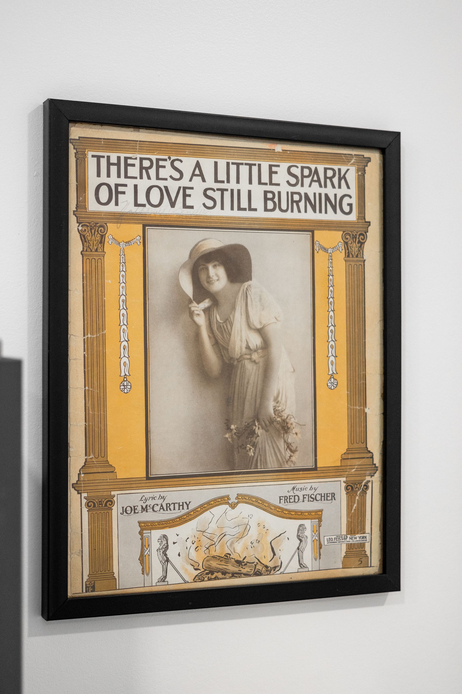 Framed vintage poster on a wall with beige, yellow, and black tones, reading “THERE’S A LITTLE SPARK OF LOVE STILL BURNING.”