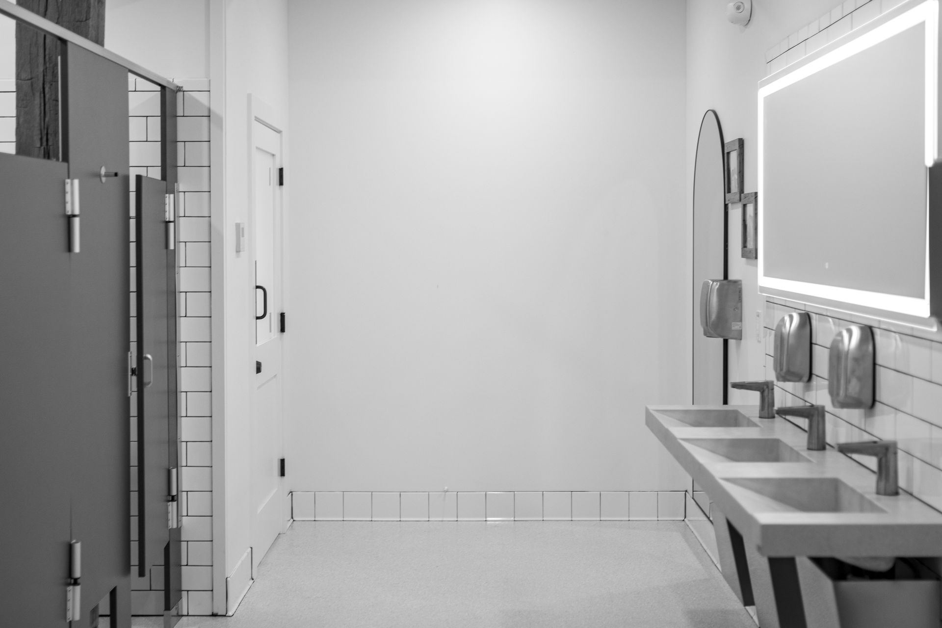Modern bathroom with stalls, sink counters, and a large mirror on the right