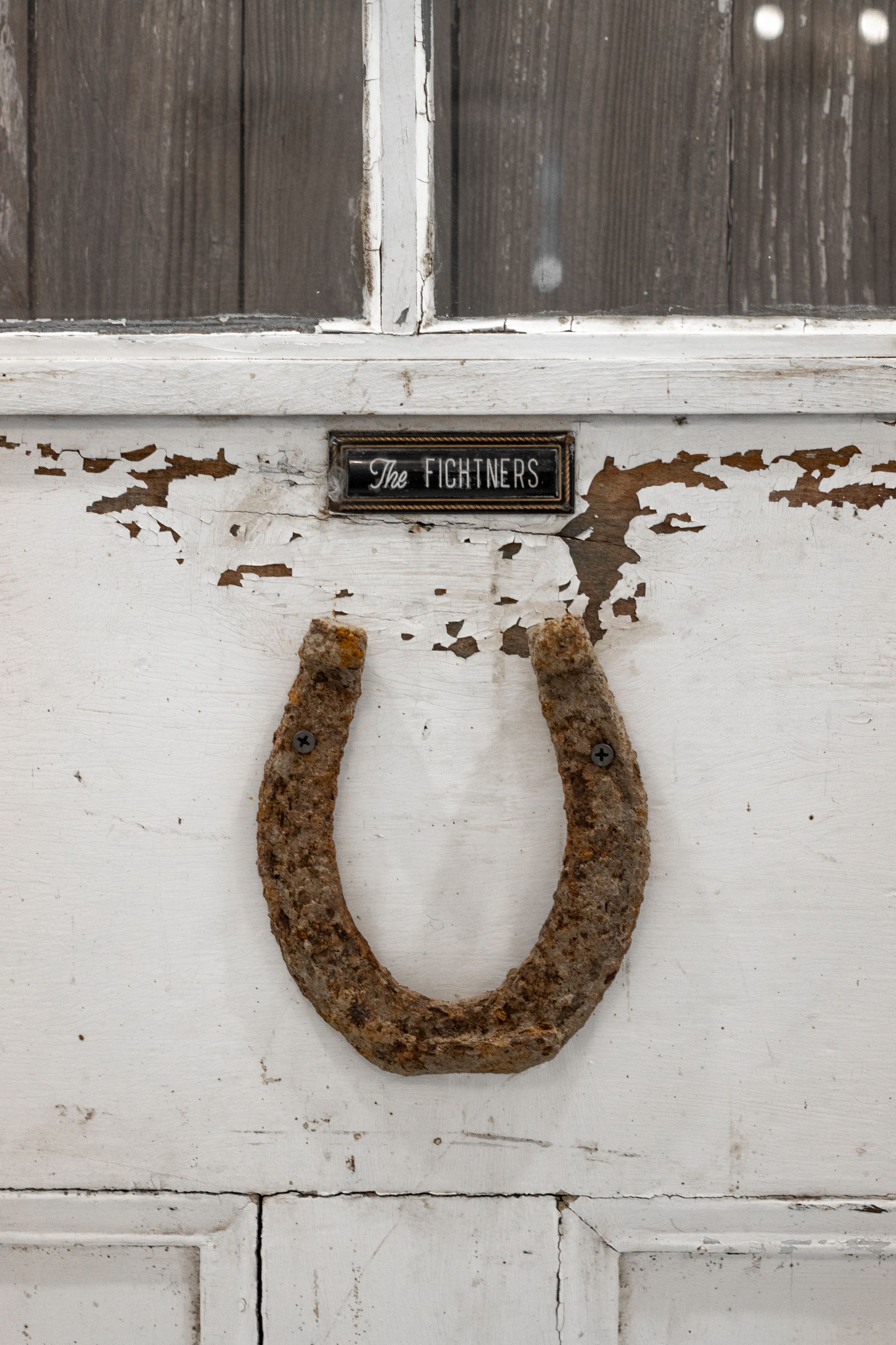 Rusty horseshoe mounted on a weathered white wooden door near a small metal nameplate.