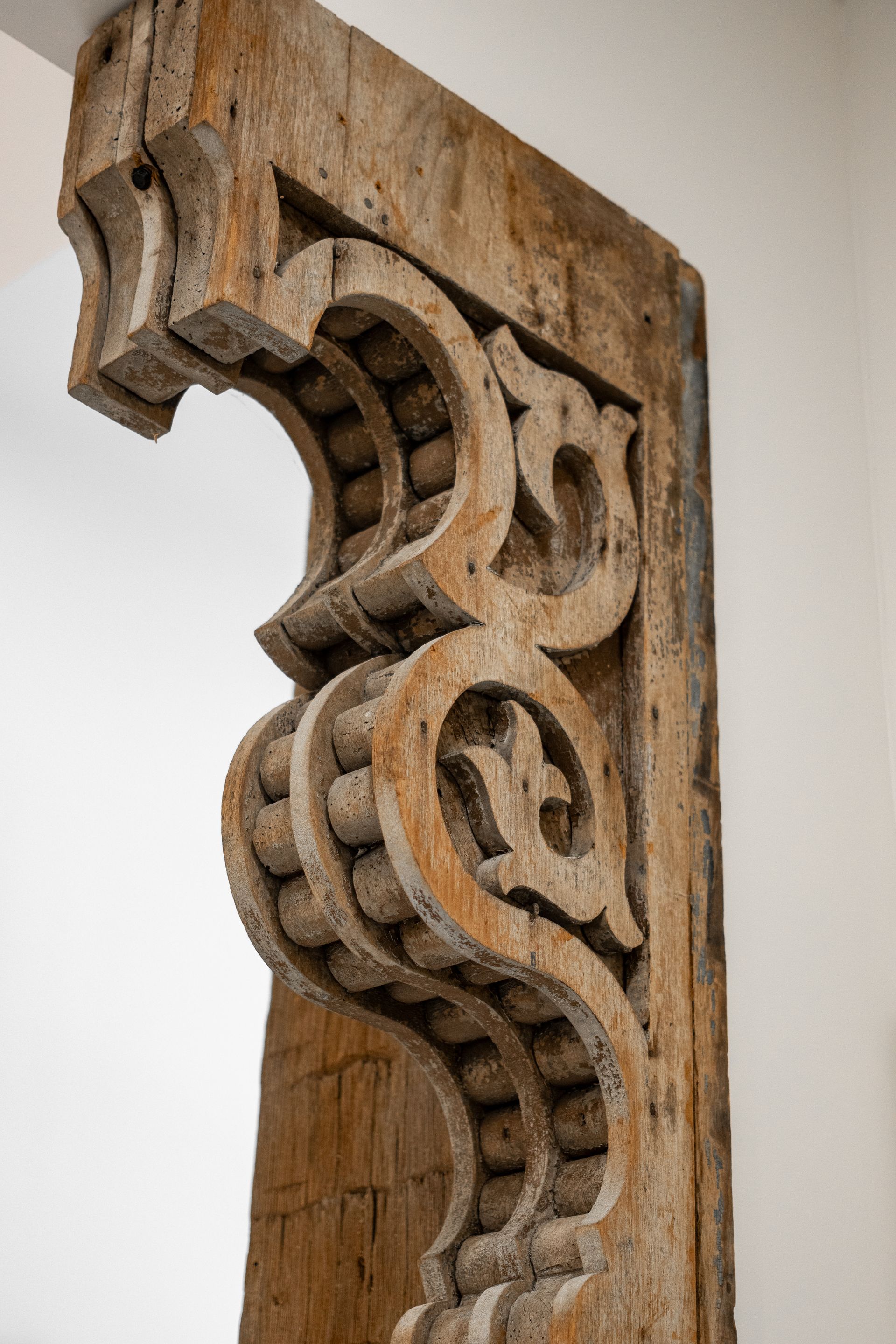 Ornate carved wooden corbel with scrolling details against a light wall