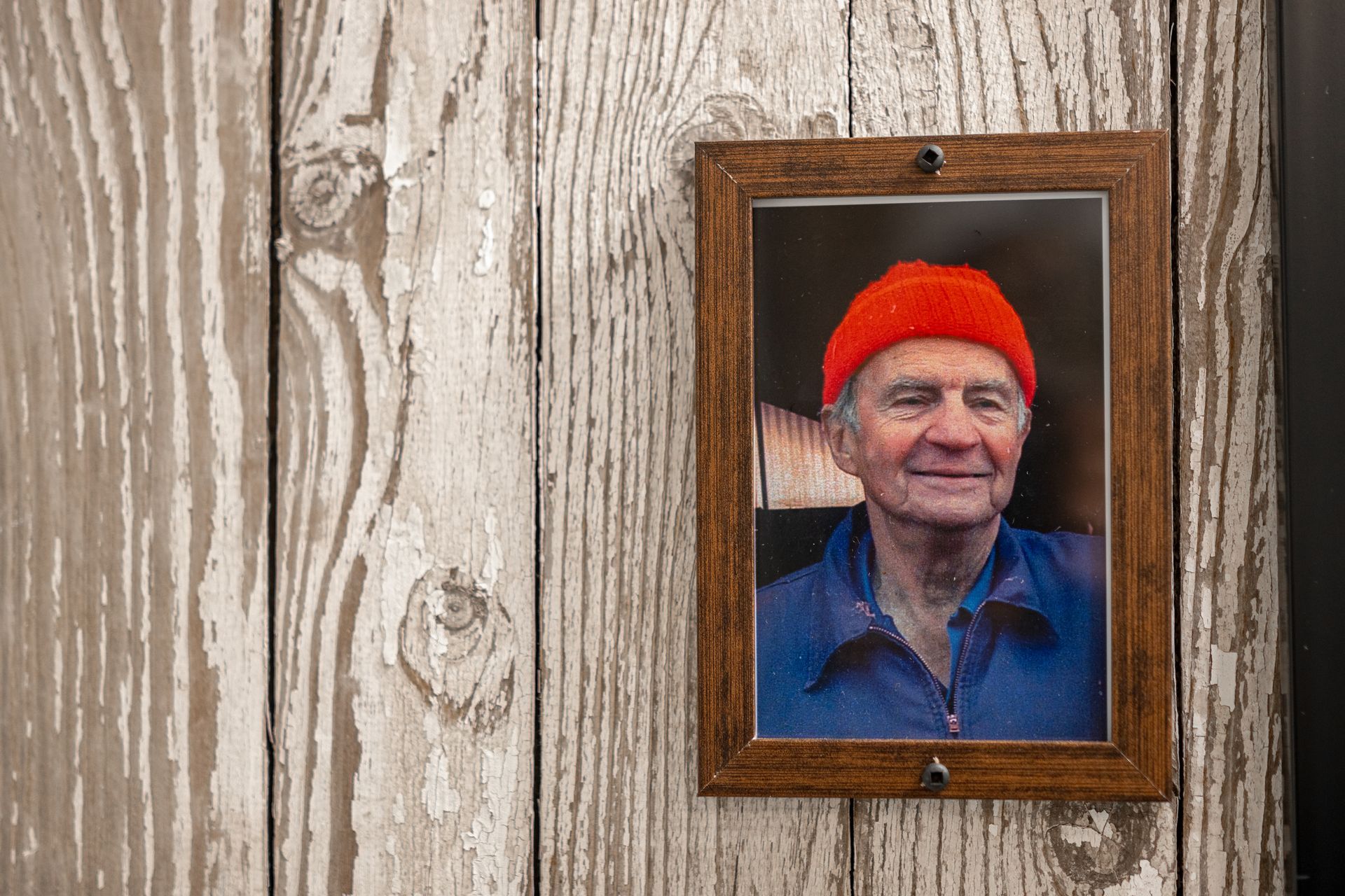Framed portrait of a smiling person in a bright orange hat on a weathered wood wall
