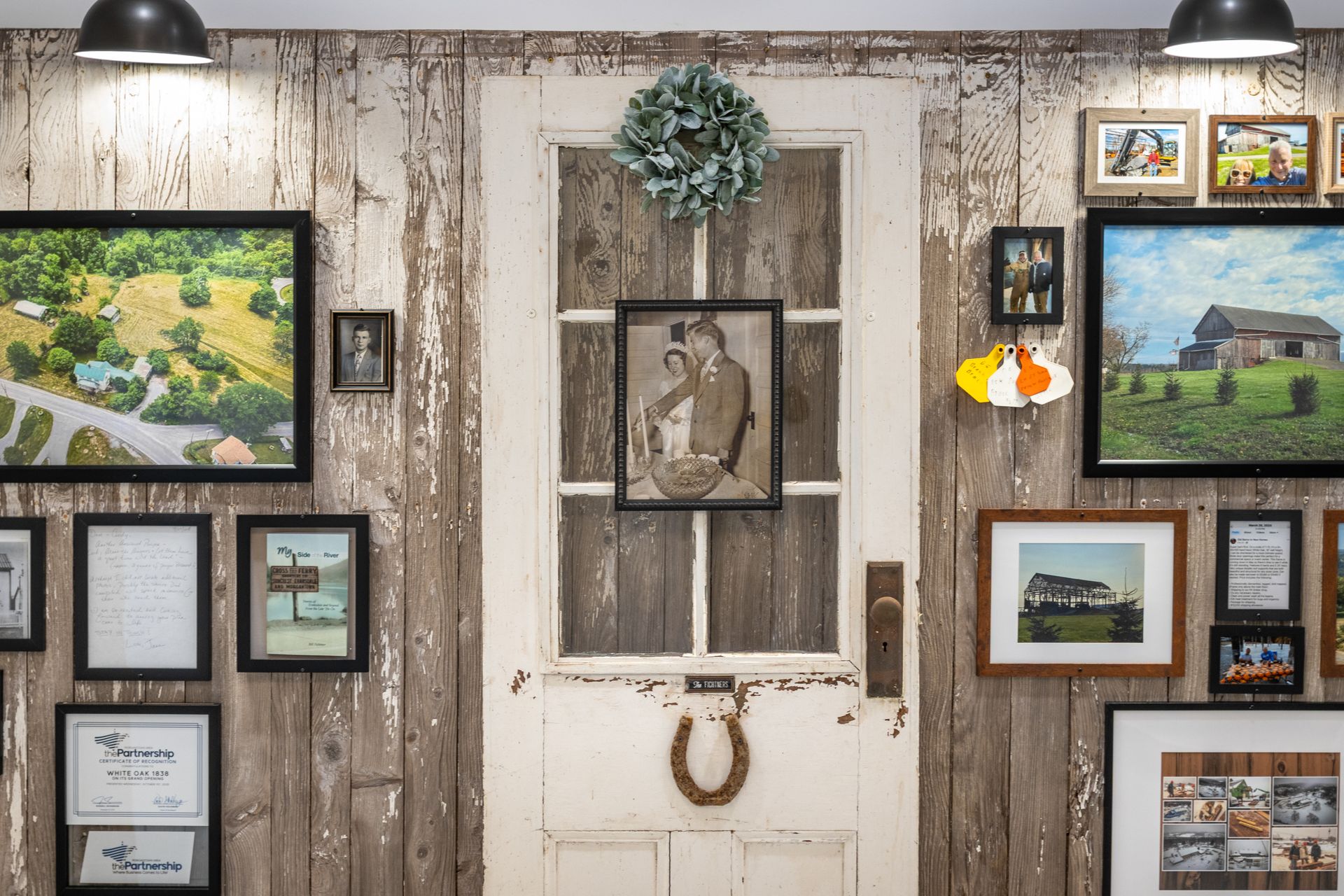 Rustic gallery wall with framed artwork around a distressed white door and wreath under hanging lights