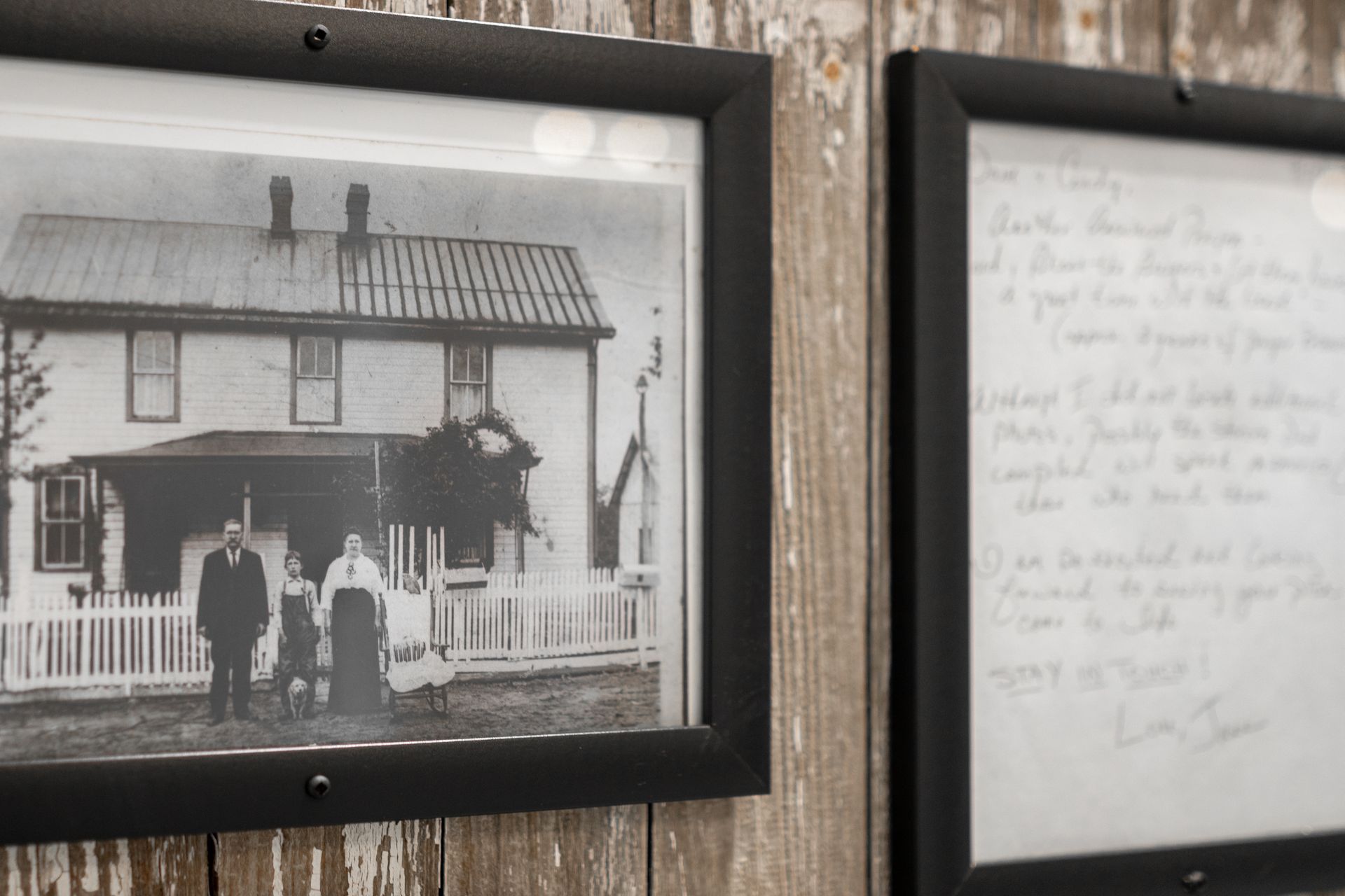 Framed black-and-white photo of people standing in front of a house, next to a handwritten note