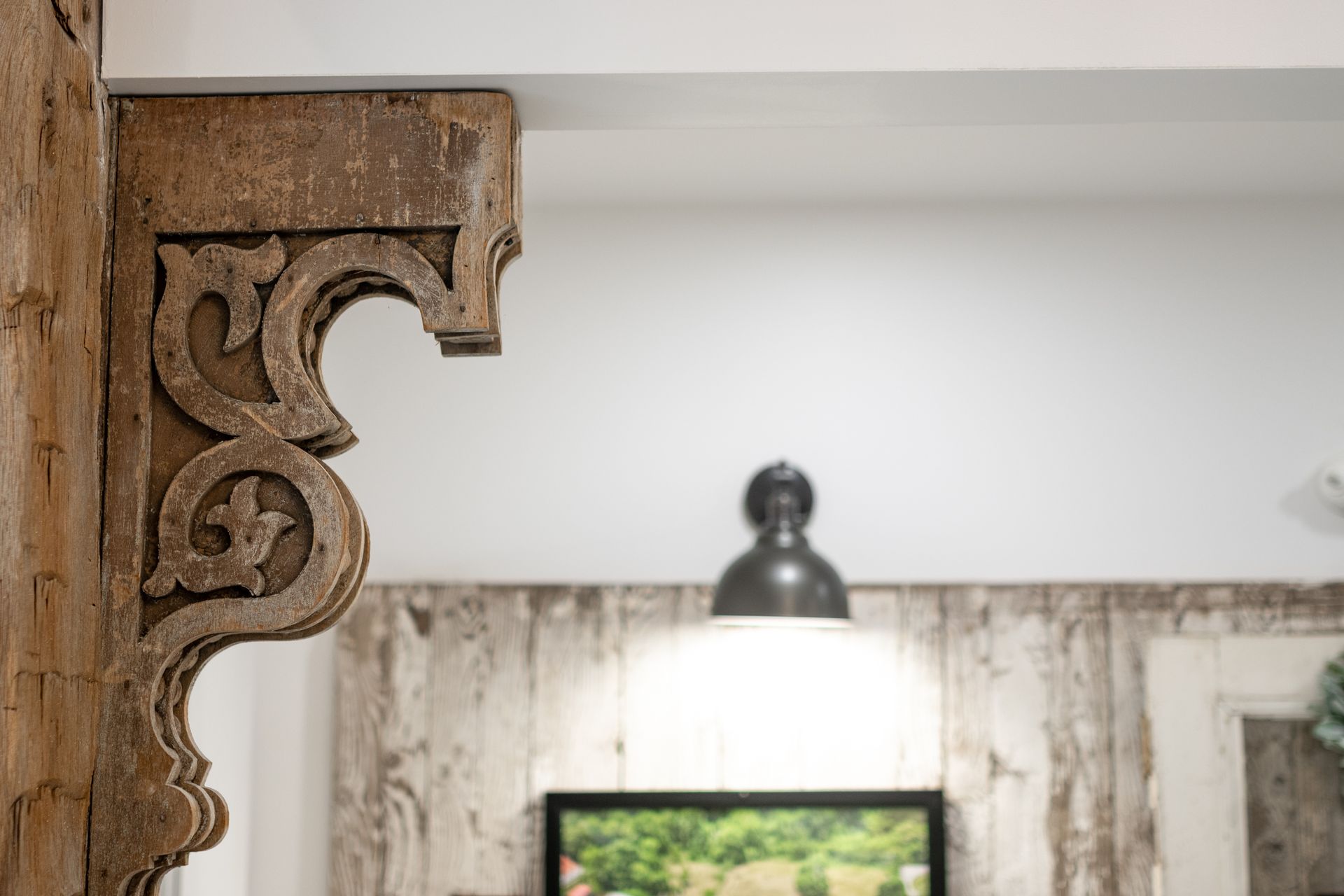 Close-up of ornate wooden corbel beside a lit wall sconce in a rustic interior