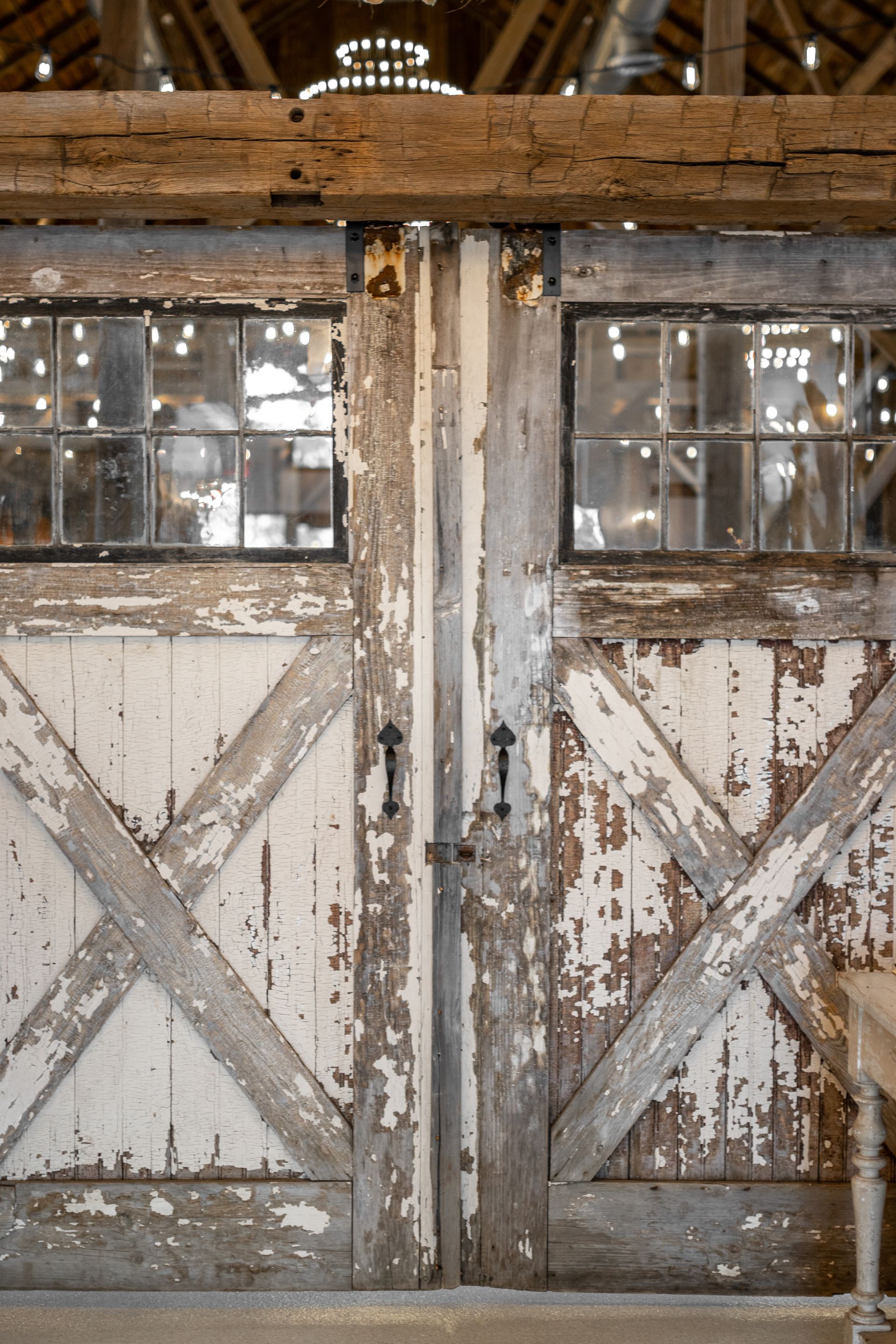 Weathered white barn doors with rusted X-braces and small windows in a rustic interior