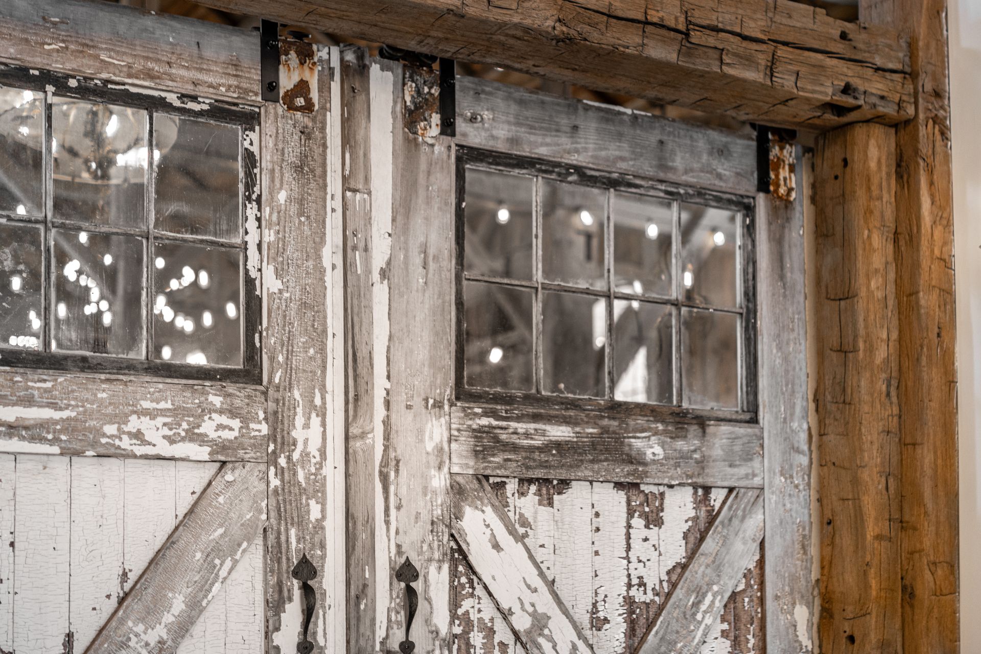 Weathered white barn doors with small windows and peeling paint on a rustic wooden wall.