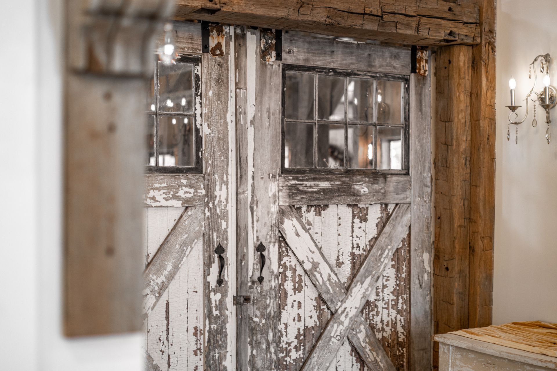 Rustic white barn doors with X-bracing and small windows under a wooden beam in a weathered interior