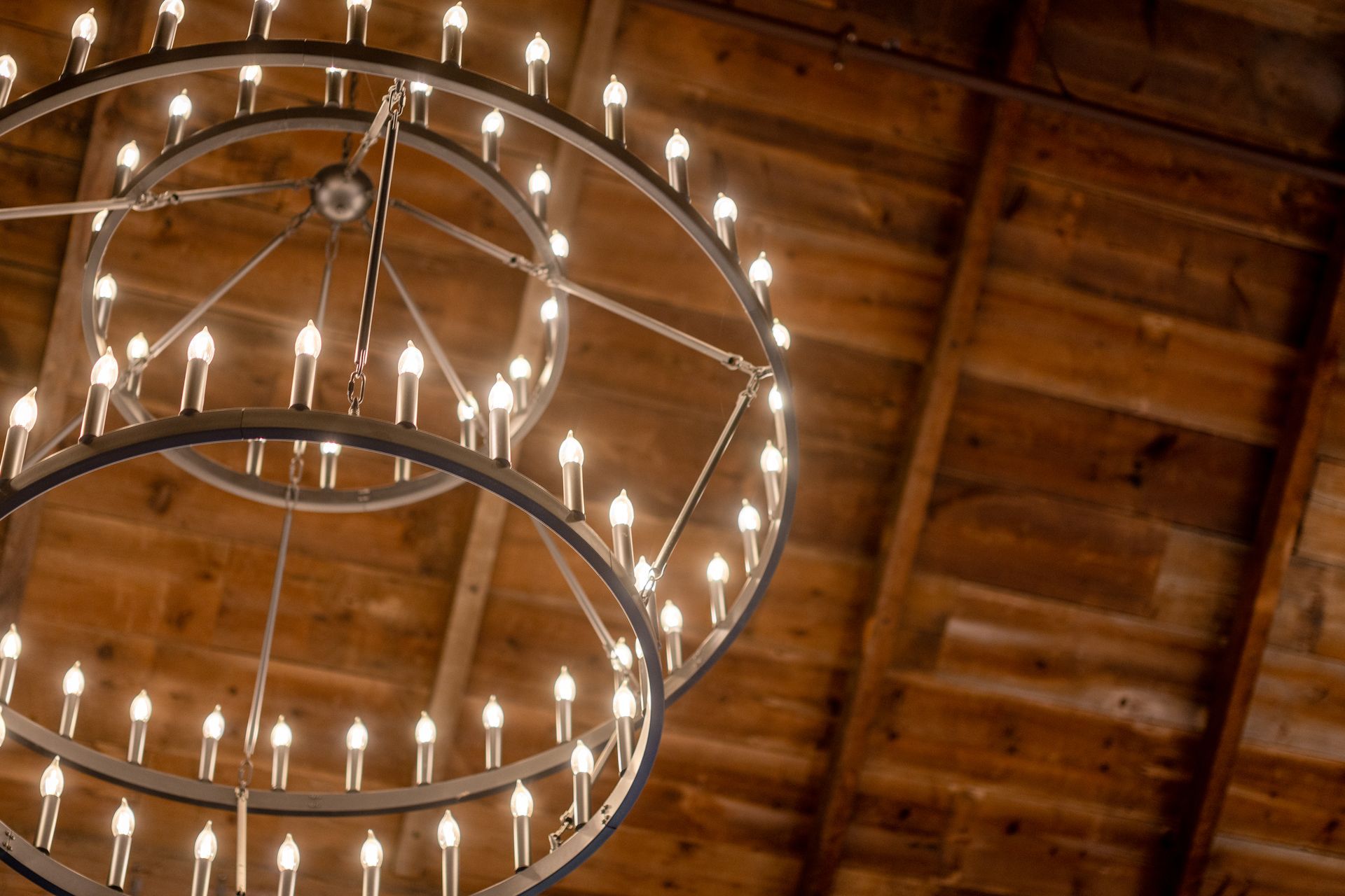 Two glowing circular chandeliers hanging from a wooden ceiling indoors