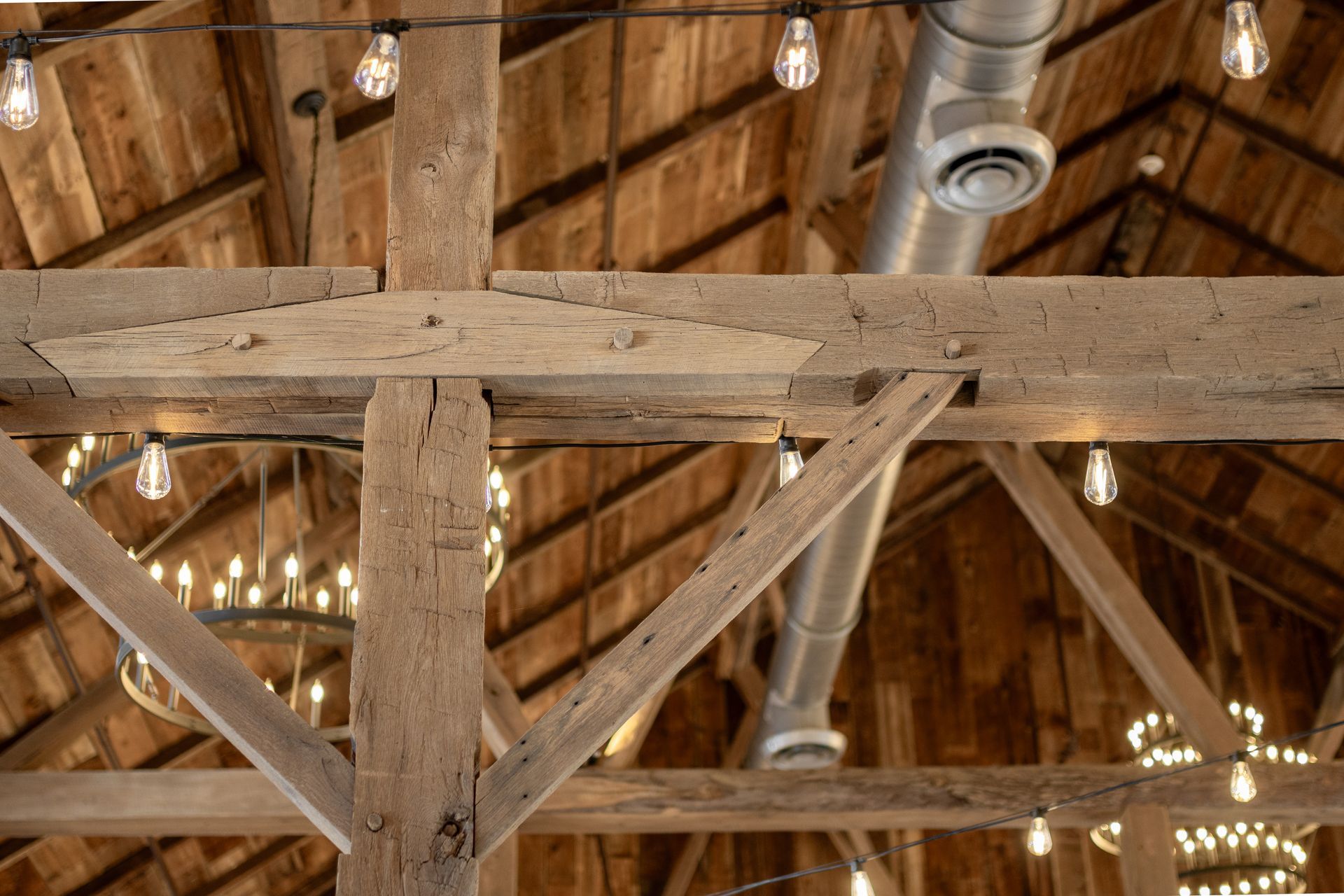 Rustic wooden barn ceiling with exposed beams, hanging lights, and a metal duct.