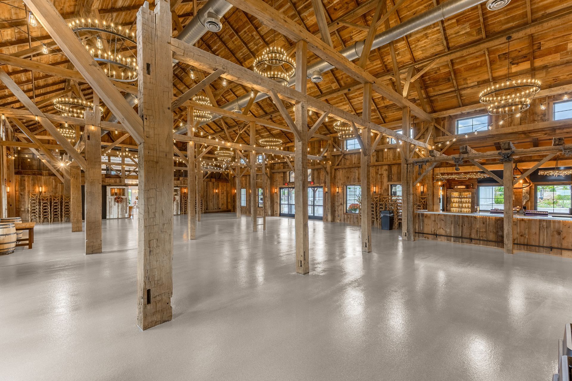 Large, empty barn interior with wooden beams, chandeliers, and glossy white floor.