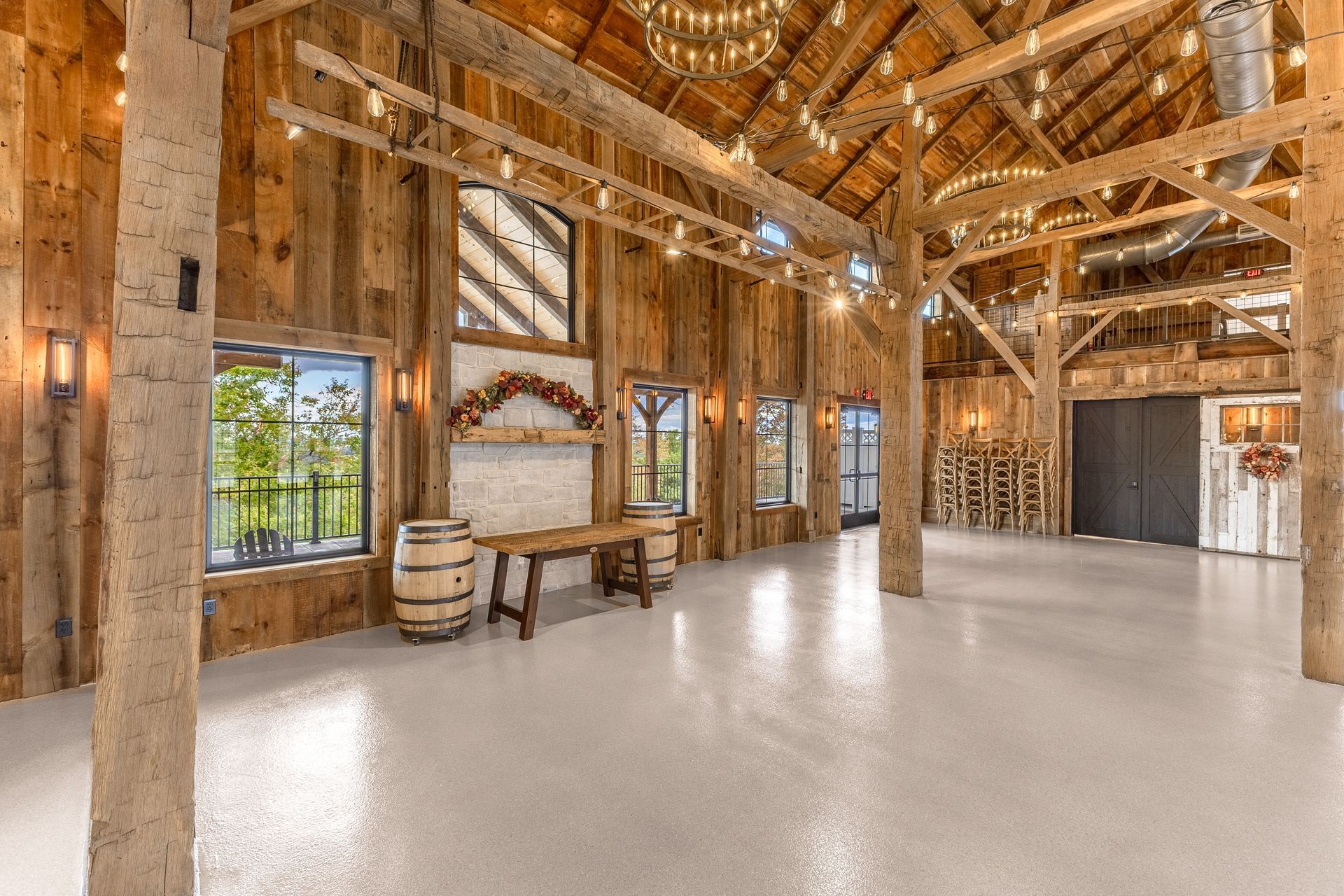 Rustic barn-style event hall with exposed beams, white floor, and windows letting in natural light