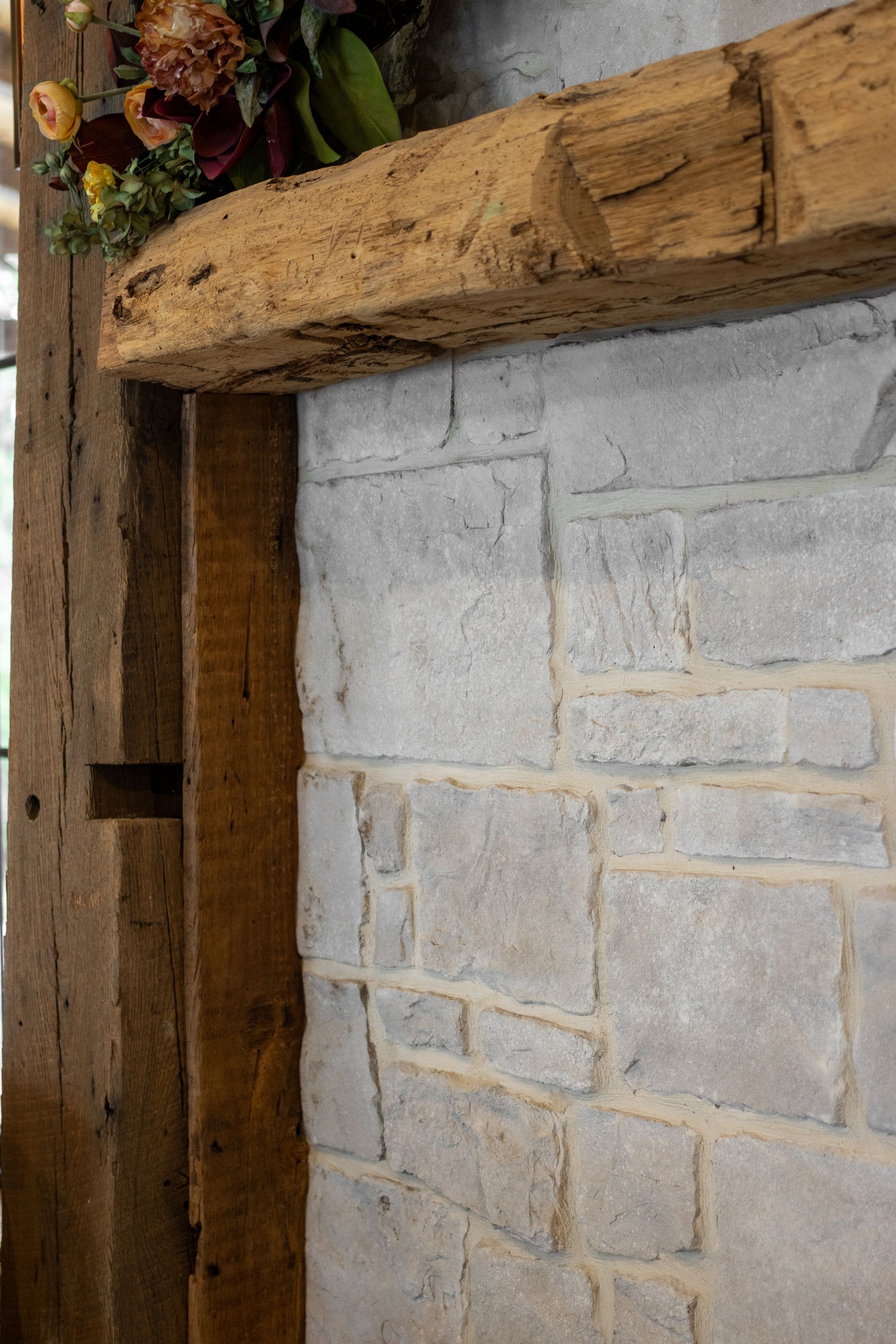 Rustic wooden beam and stone wall corner with a small floral arrangement above.