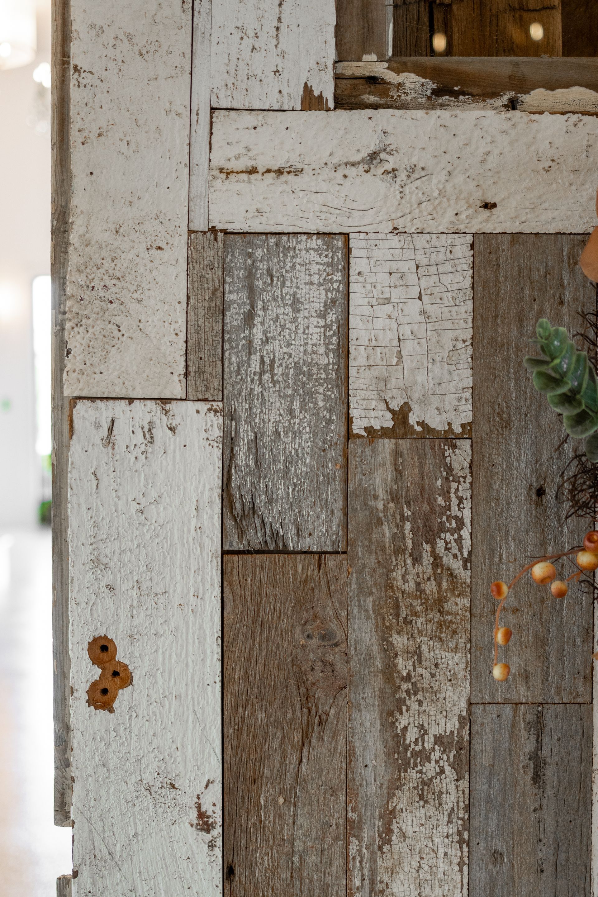 Weathered white wooden wall with peeling paint, narrow windows, and small orange flowers on the right
