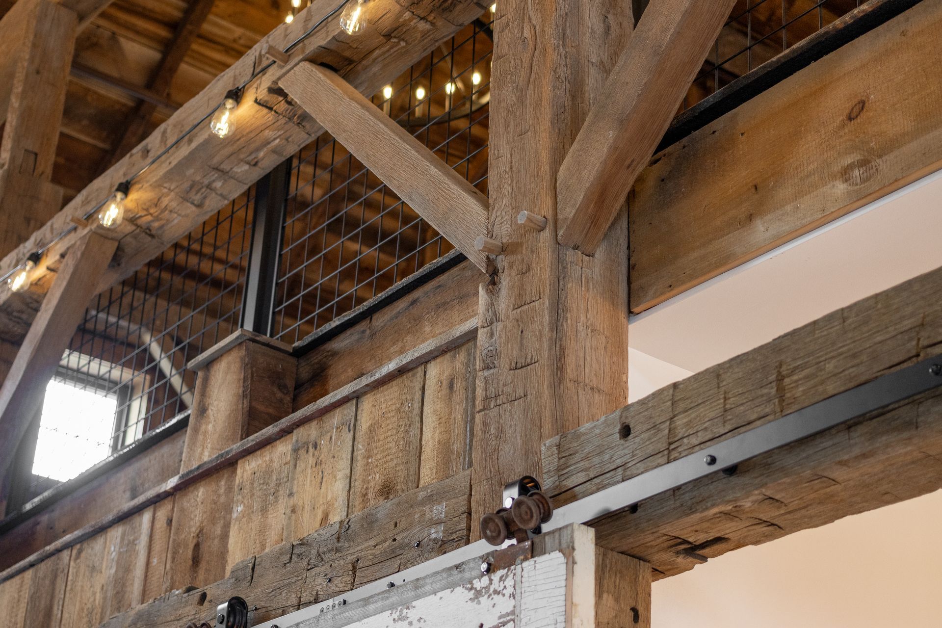 Rustic barn interior with wooden beams, string lights, and a lofted walkway