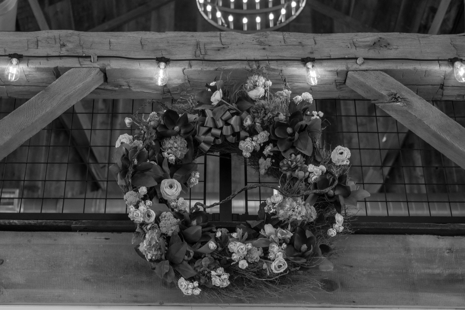 Floral wreath with white flowers and greenery hanging on a rustic wooden barn wall with a chandelier above