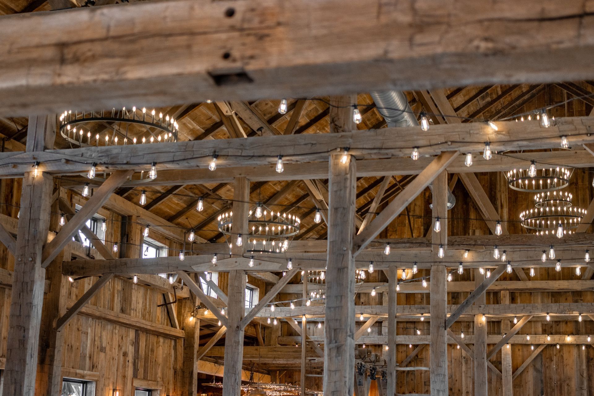 Interior of a rustic barn with exposed wooden beams and hanging string lights
