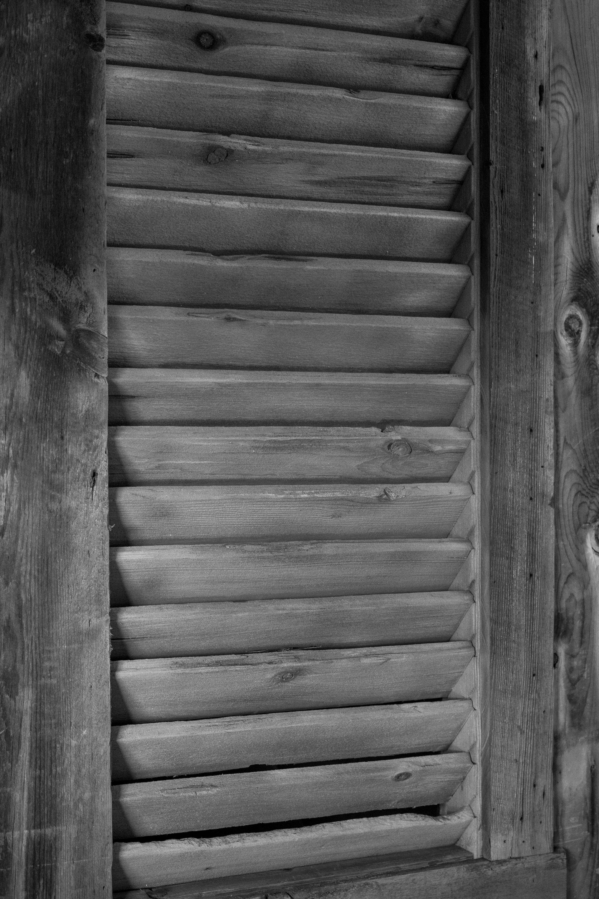 Black-and-white close-up of a weathered wooden louvered window shutter.