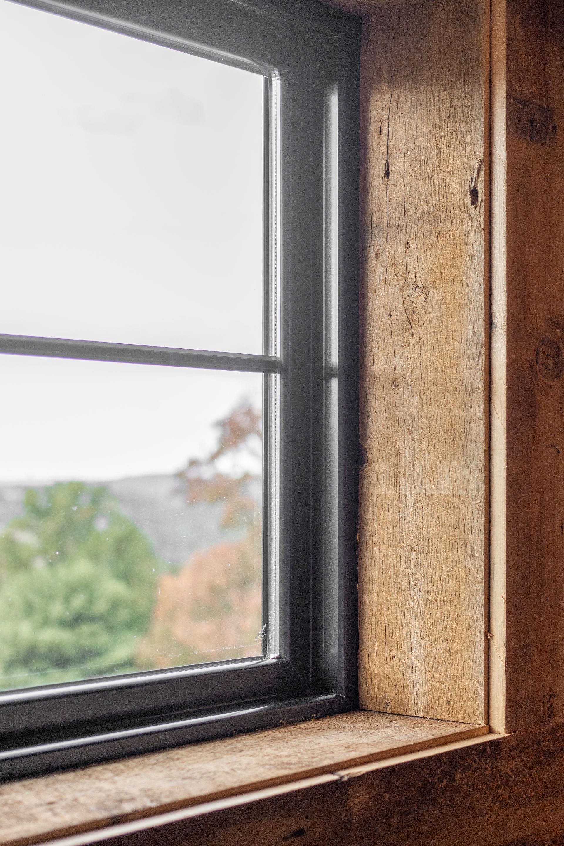 Wooden window frame with a black pane, showing a blurry outdoor view and daylight.
