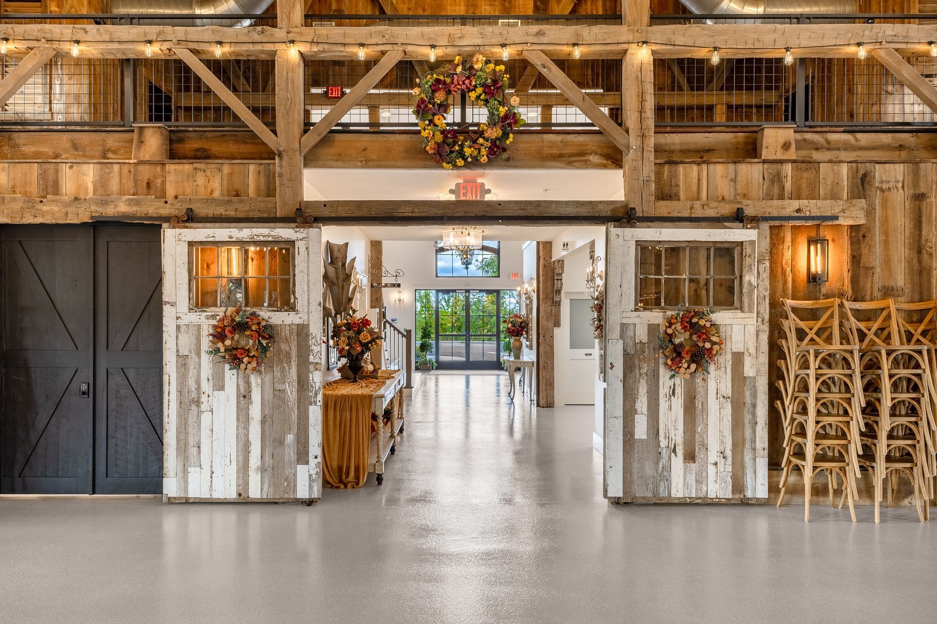 Rustic barn interior with white double doors, floral wreaths, and a central aisle leading to a lit entrance