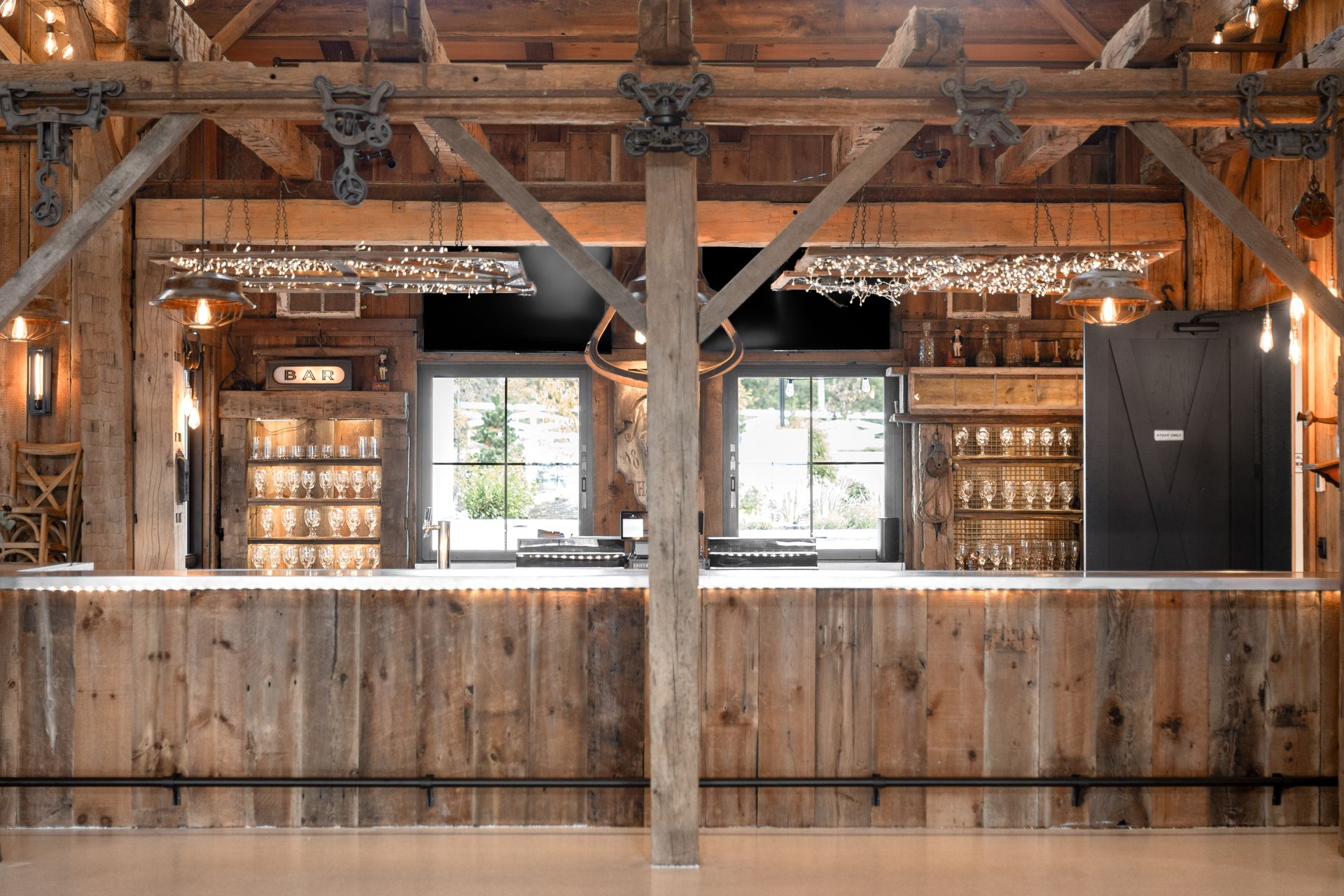 Rustic wooden bar interior with exposed beams, hanging lights, and shelves of bottles behind the counter.