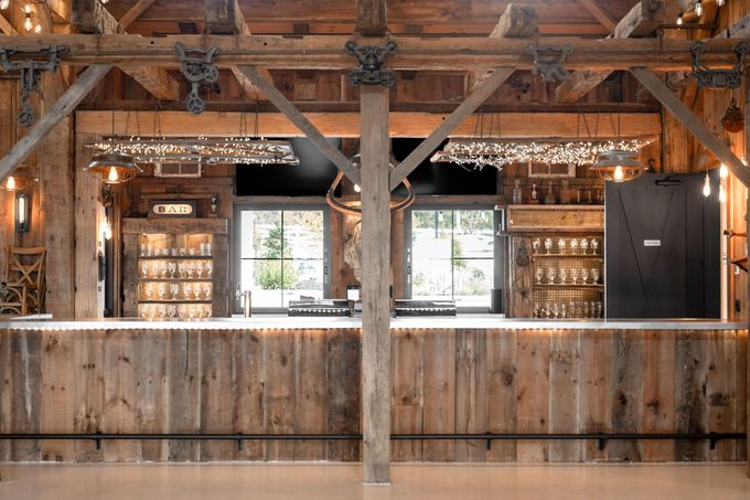 Rustic wooden bar inside a barn with string lights, glassware, and two large windows.