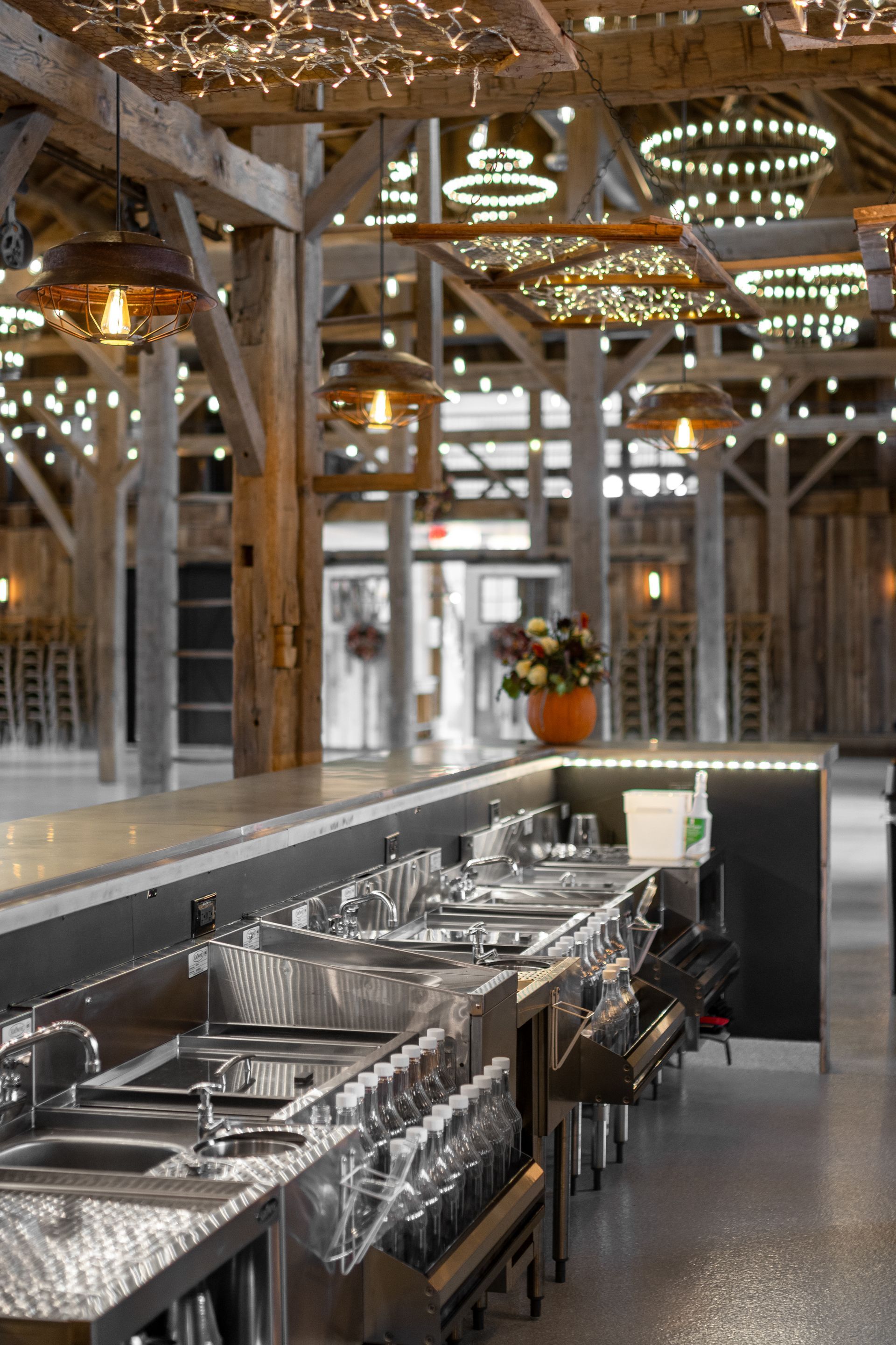 Rustic restaurant bar with shiny sinks and exposed wooden beams under warm hanging lights.