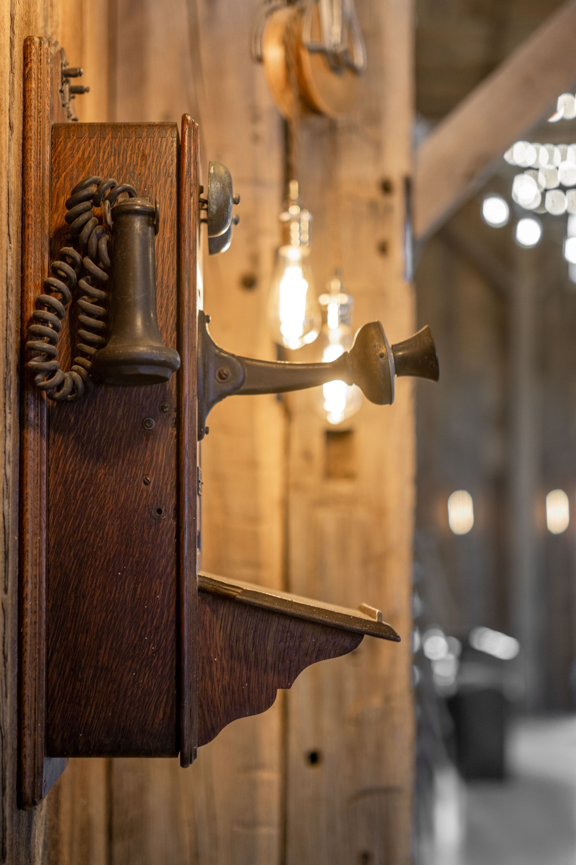 Rusty metal industrial latch on a wooden door, with warm hanging lights and a blurred corridor in the background