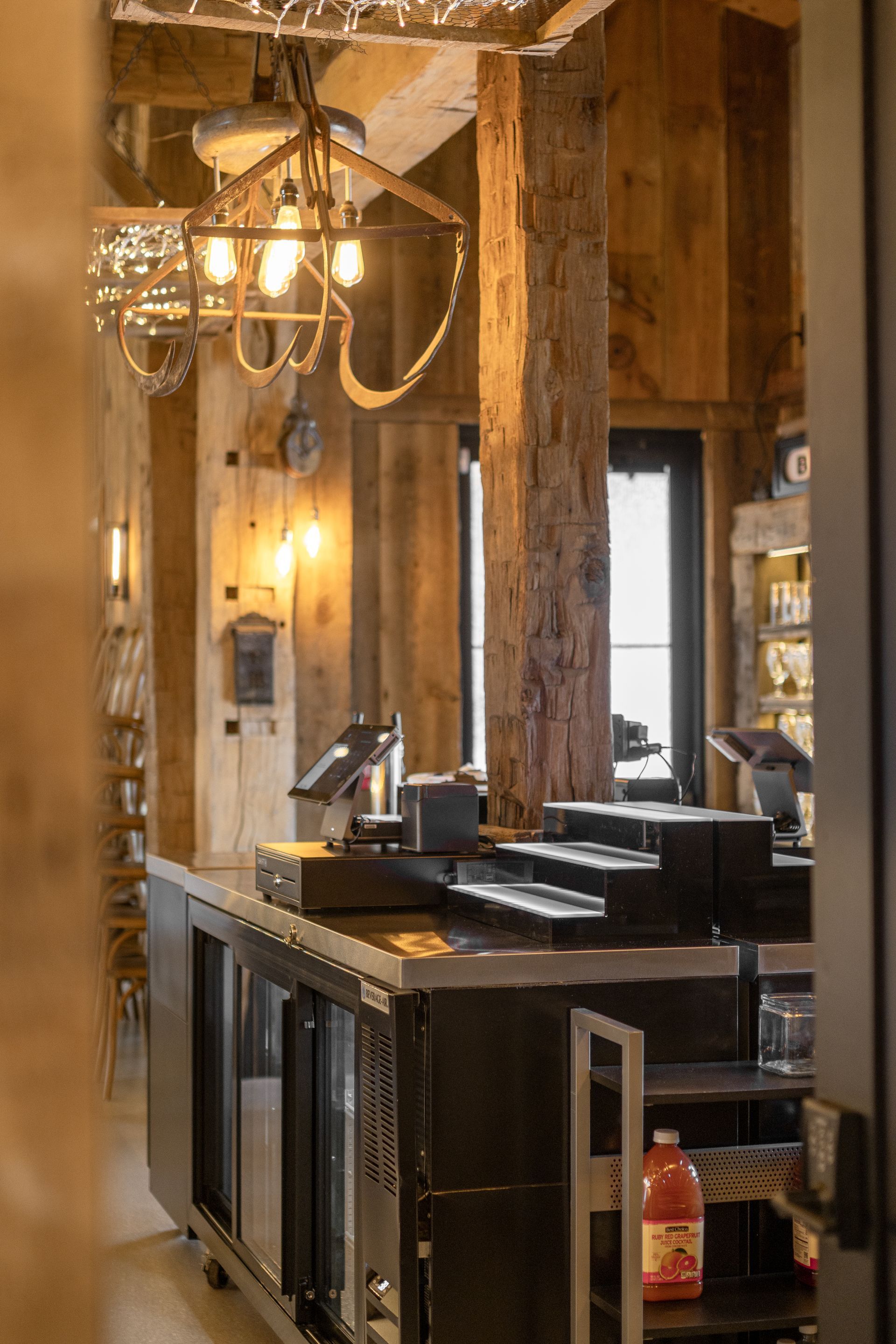 Warm rustic restaurant interior with a chandelier, wooden beams, and a service counter.