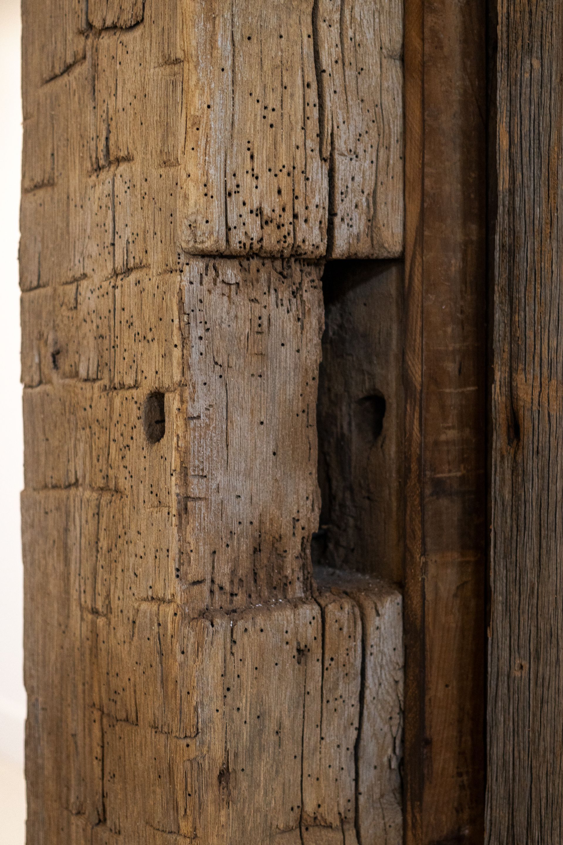 Close-up of weathered wooden post with carved notches and a dark vertical groove