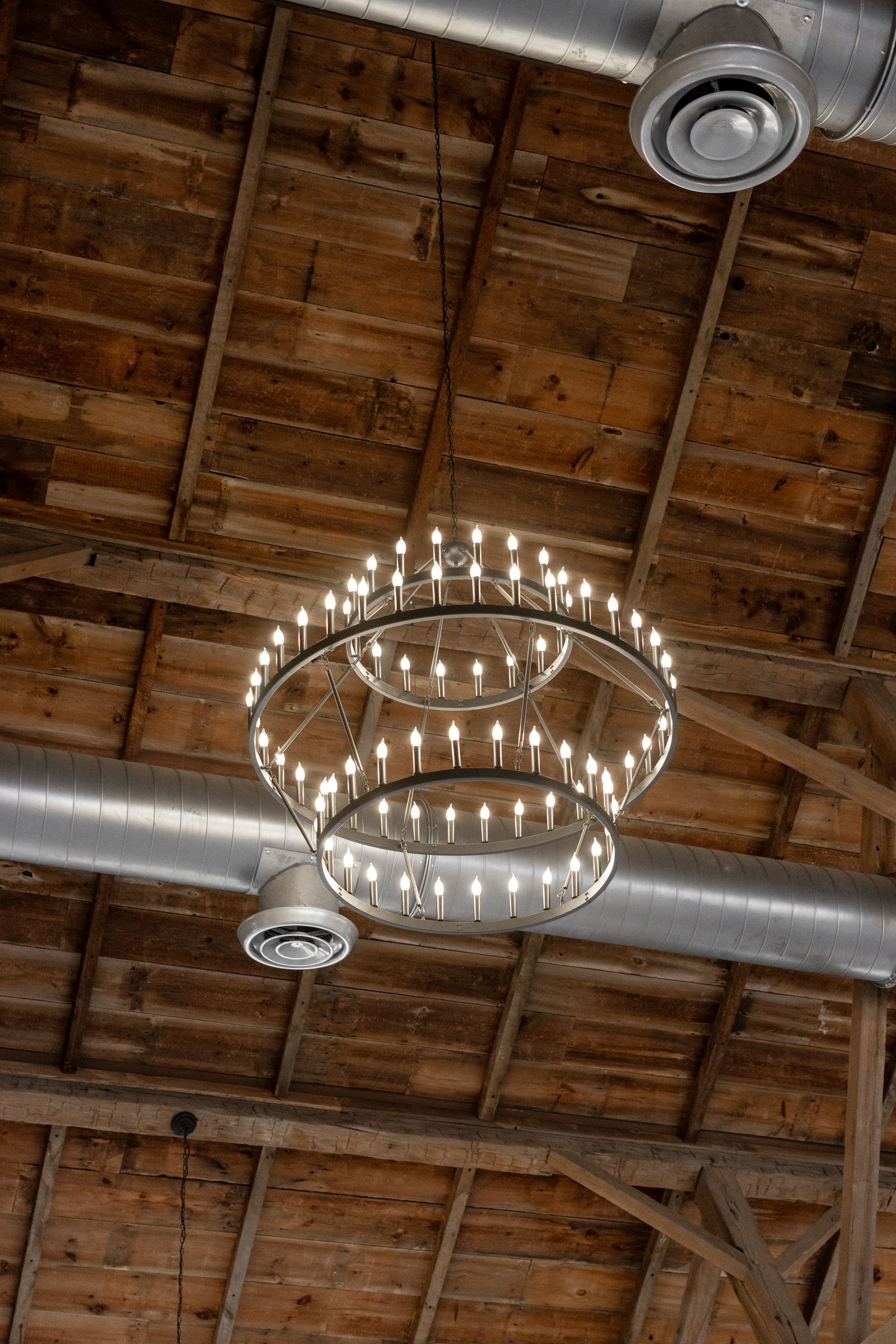Chandelier hanging from a rustic wooden ceiling with exposed beams and silver ductwork