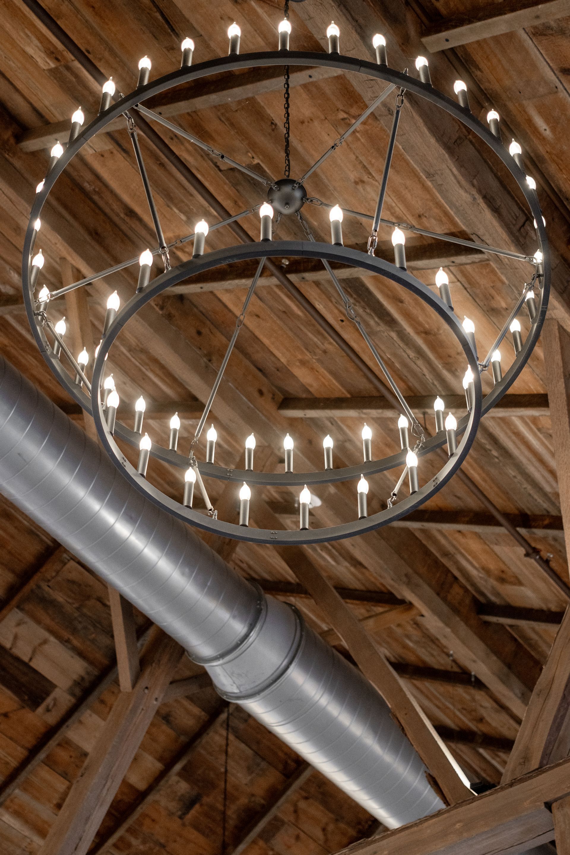 Two-tier chandelier hanging from a rustic wooden ceiling with exposed metal ductwork