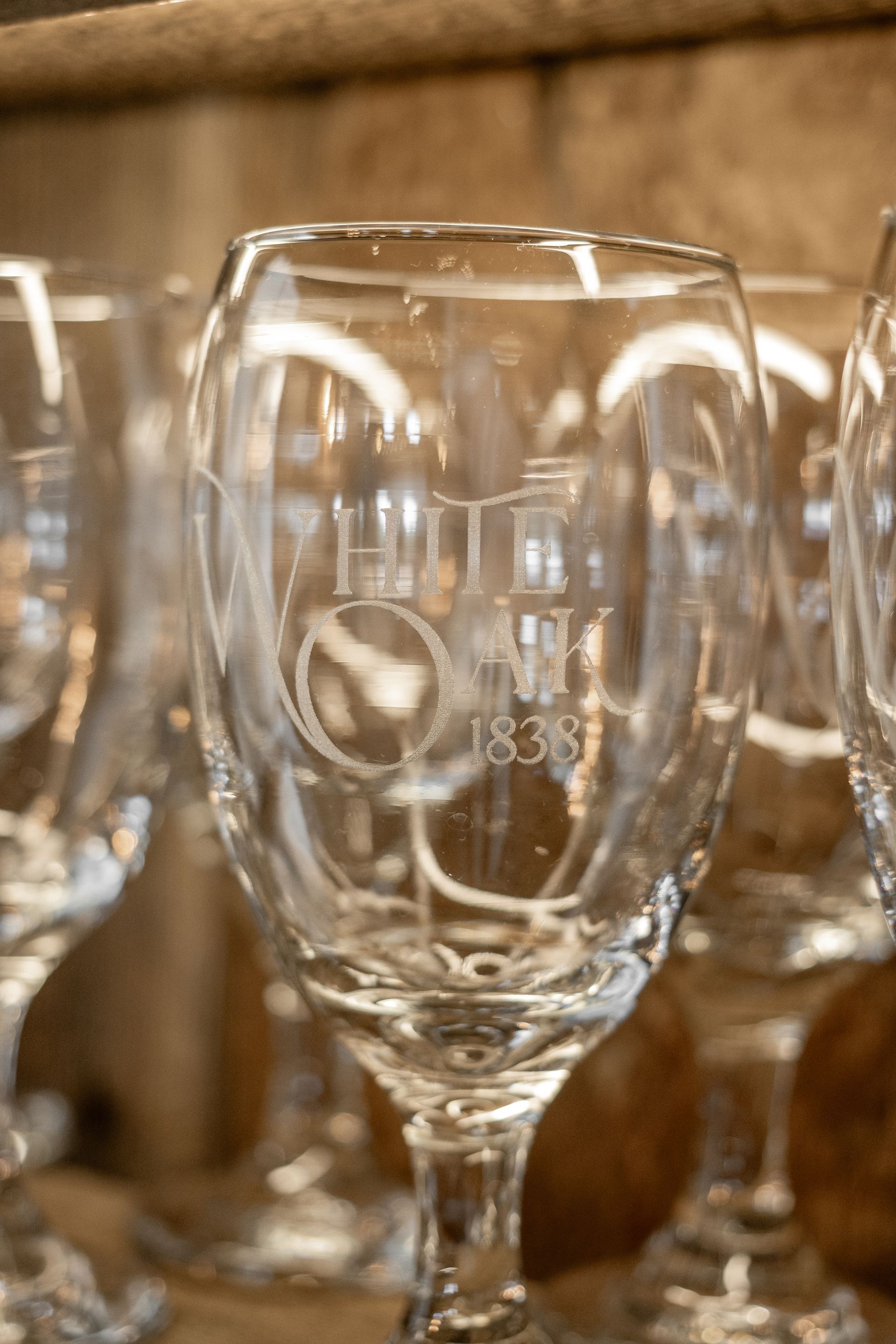 Clear wine glasses lined up on a shelf, reflecting warm light.