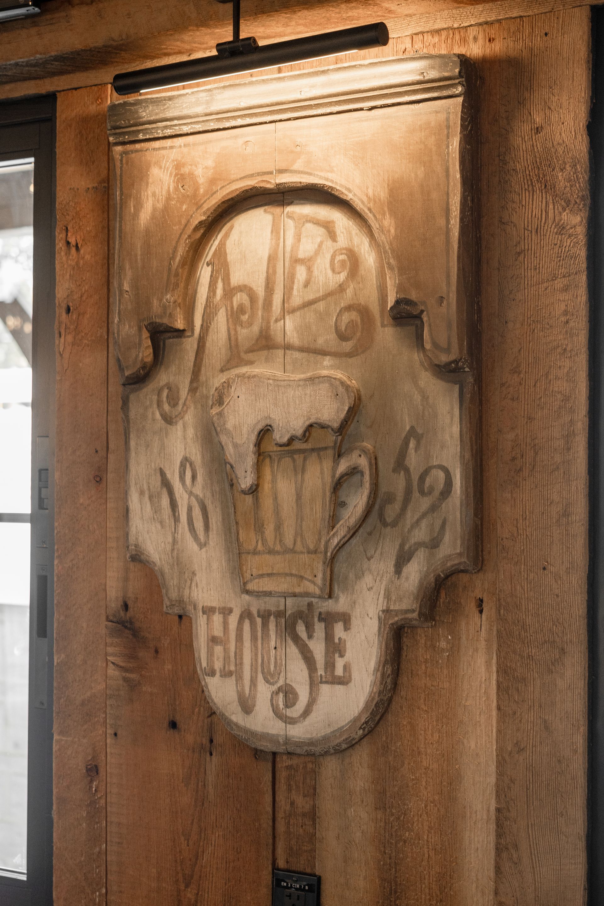 Vintage carved wooden plaque on a door, with faded lettering and a central raised emblem.