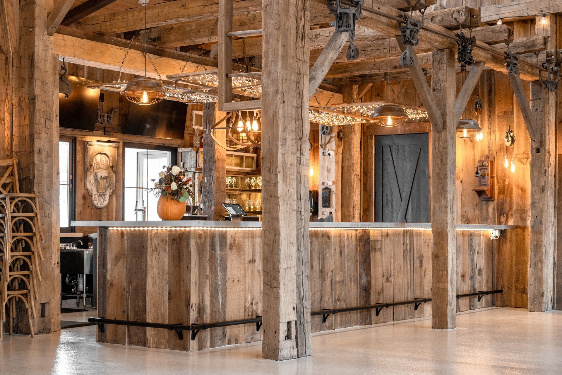 Rustic restaurant interior with wooden beams, bar counter, warm lights, and hanging decor