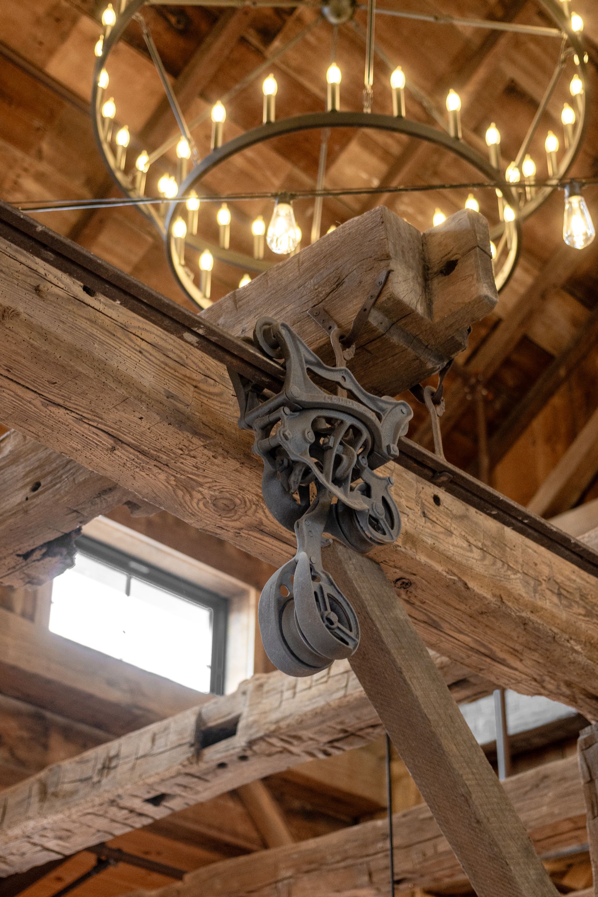 Close-up of a rustic wooden beam and metal pulley under a chandelier in a barn-like interior