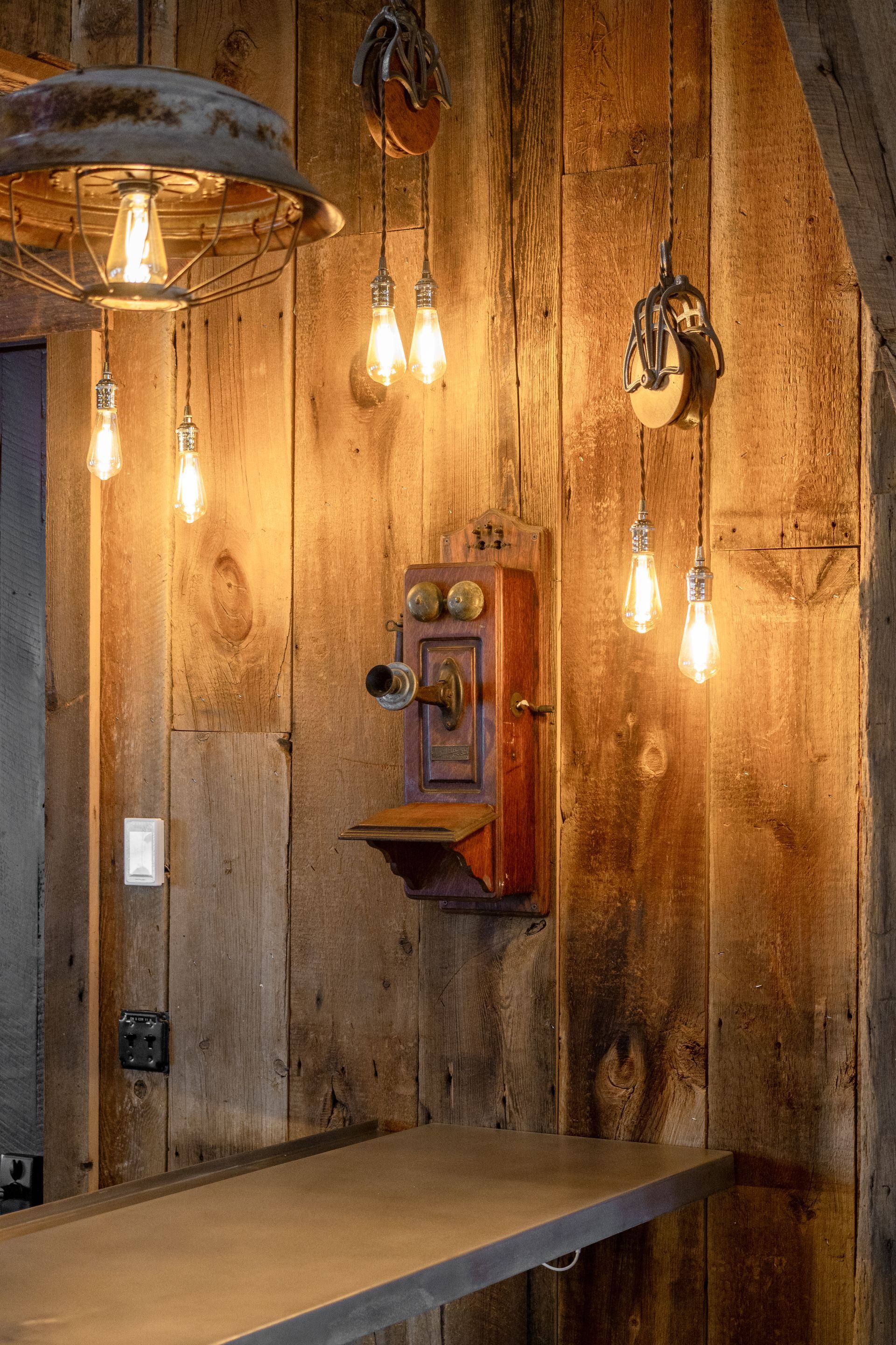 Rustic café wall with hanging Edison bulbs, a wooden phone booth, and a long bench
