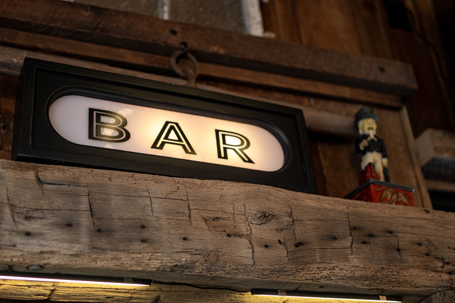 Illuminated BAR sign on a rustic wooden interior wall with a small figurine beside it