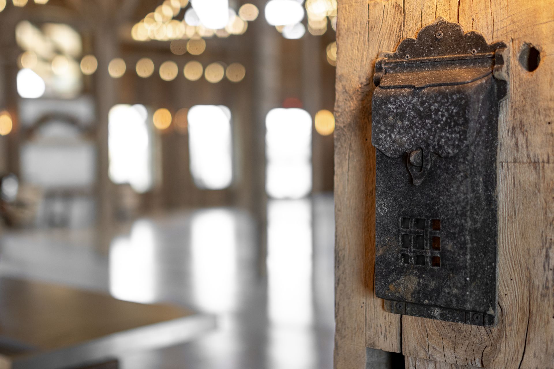 Weathered black wall-mounted electrical box on a wooden post in a blurred, sunlit interior