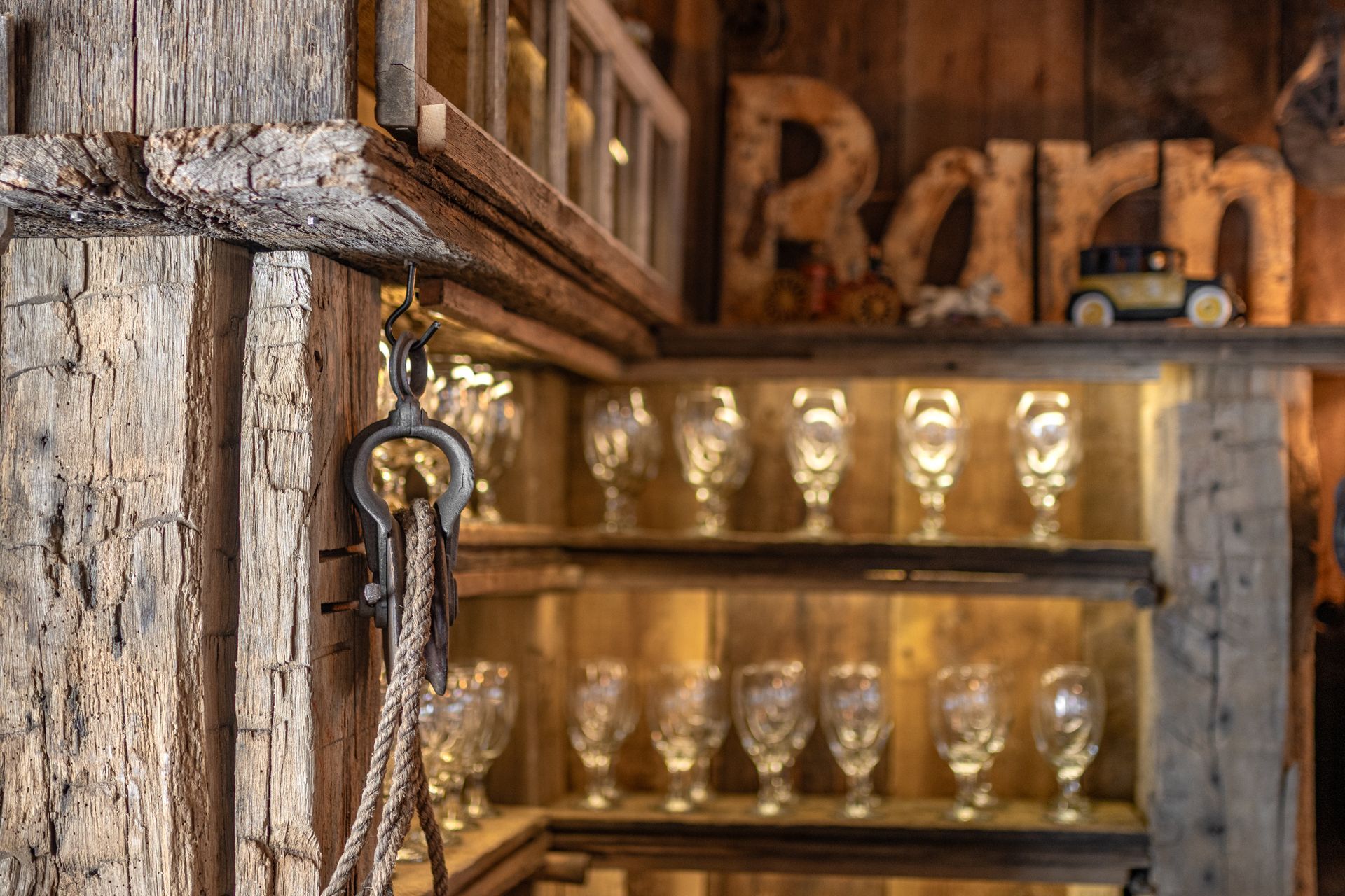 Rustic wooden shelves with rows of glasses and a hanging key against a weathered barn wall