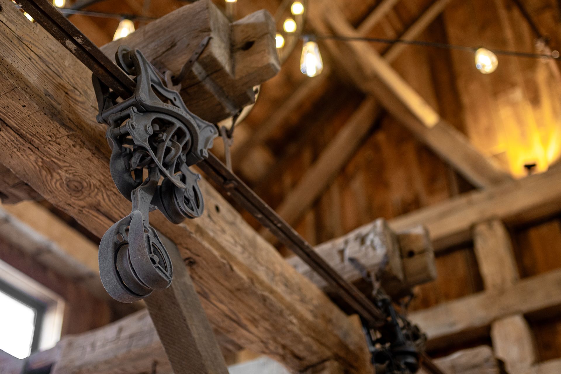 Antique pulley hoist with rope and metal wheel on wooden beams inside a rustic attic