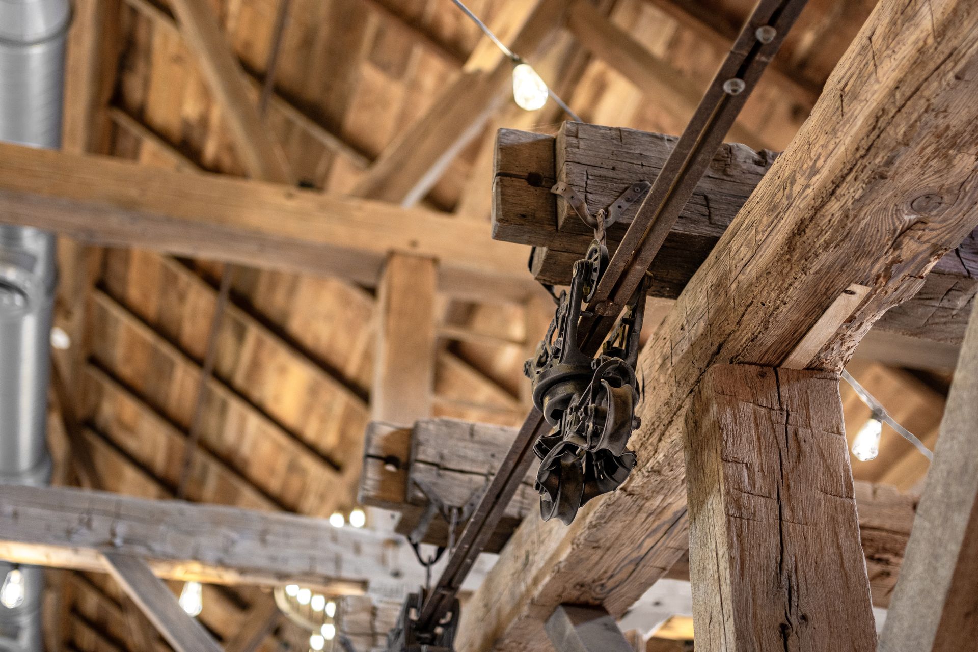 Rusty chain hoist hanging from wooden beams in an old barn interior with warm lights