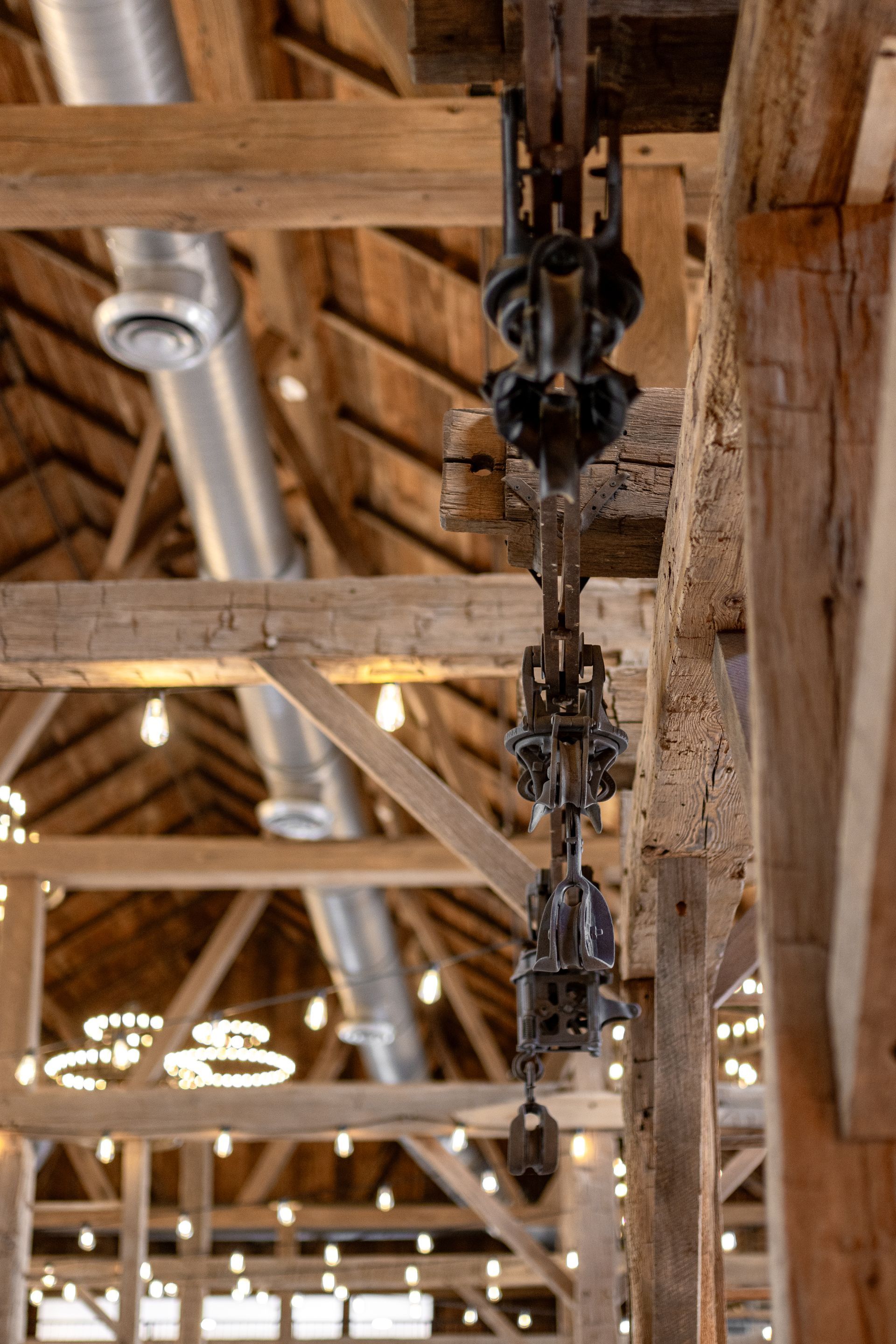 Row of hanging black industrial lights beneath rustic wooden ceiling beams in a barn-like interior