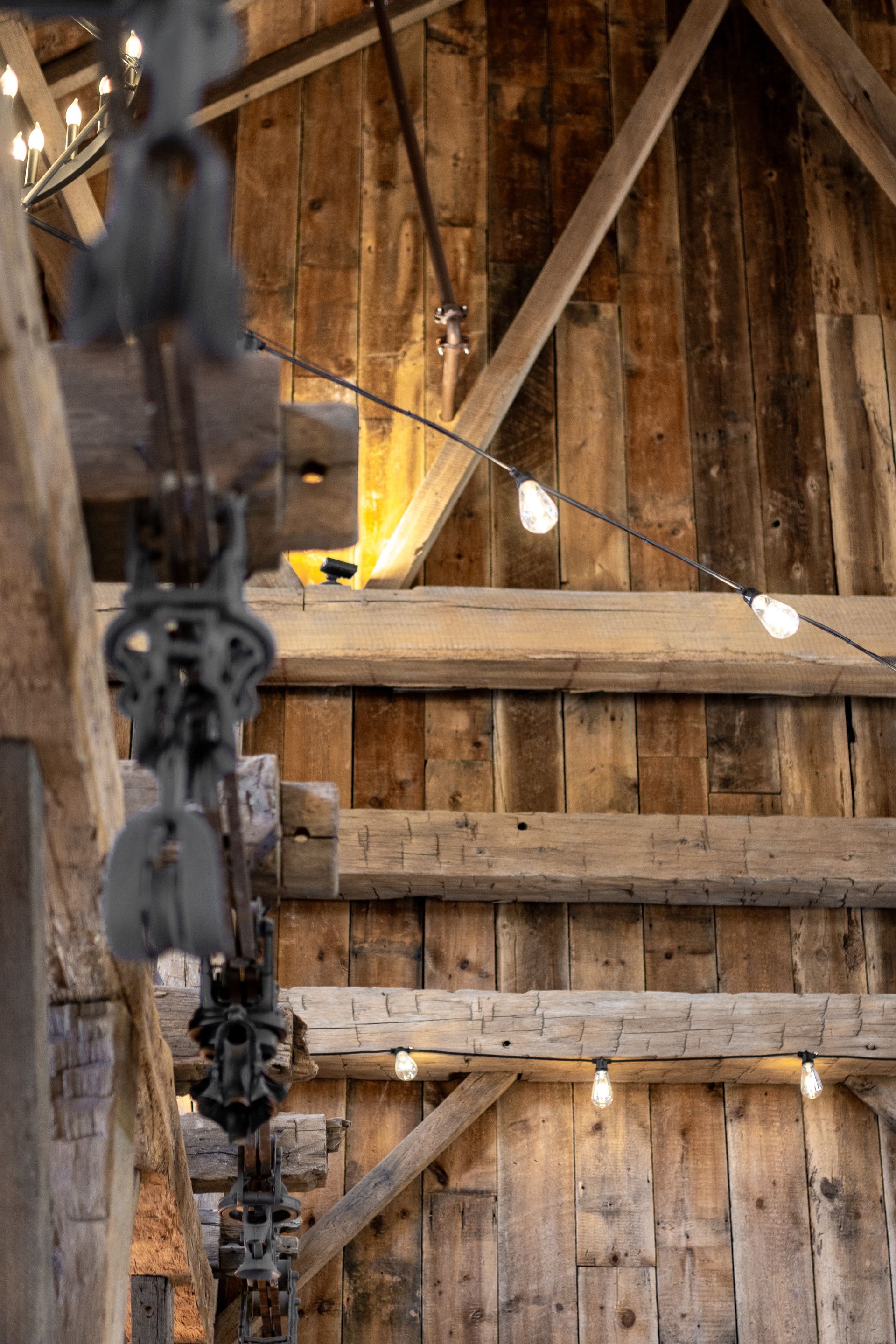 Rustic barn interior with wooden beams, hanging string lights, and a blurred chain in the foreground