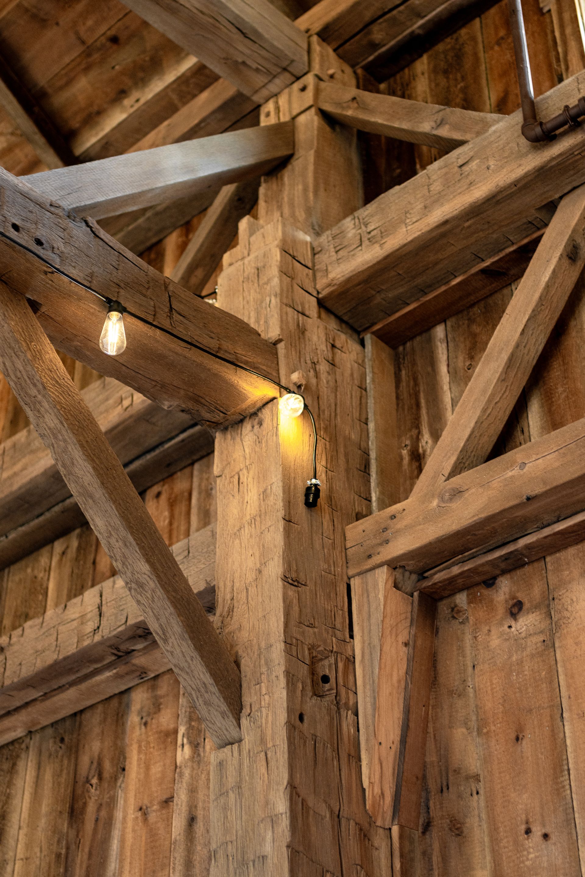 Rustic wooden barn interior with heavy beams and warm light from a wall sconce.