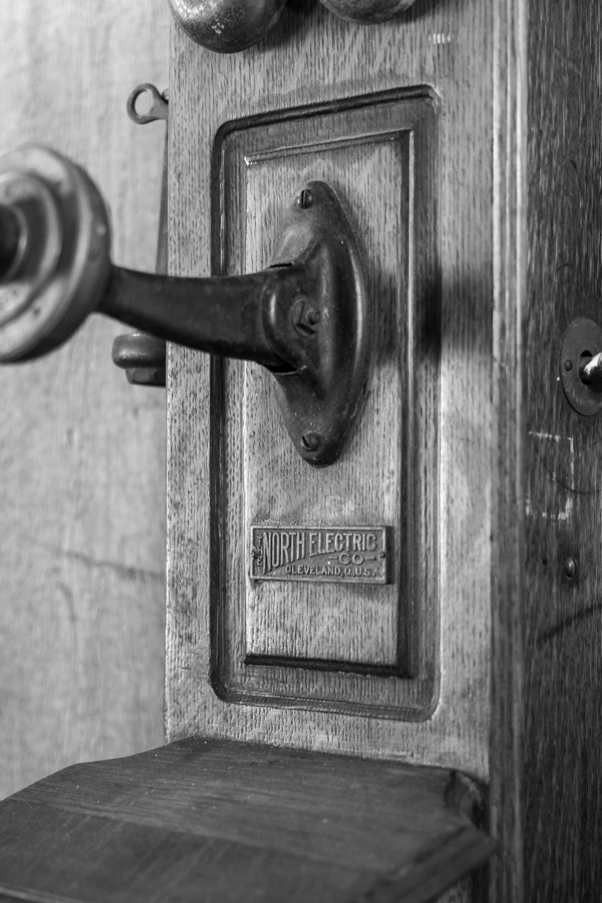 Close-up of an old metal hand-crank on a wooden wall panel, black and white.