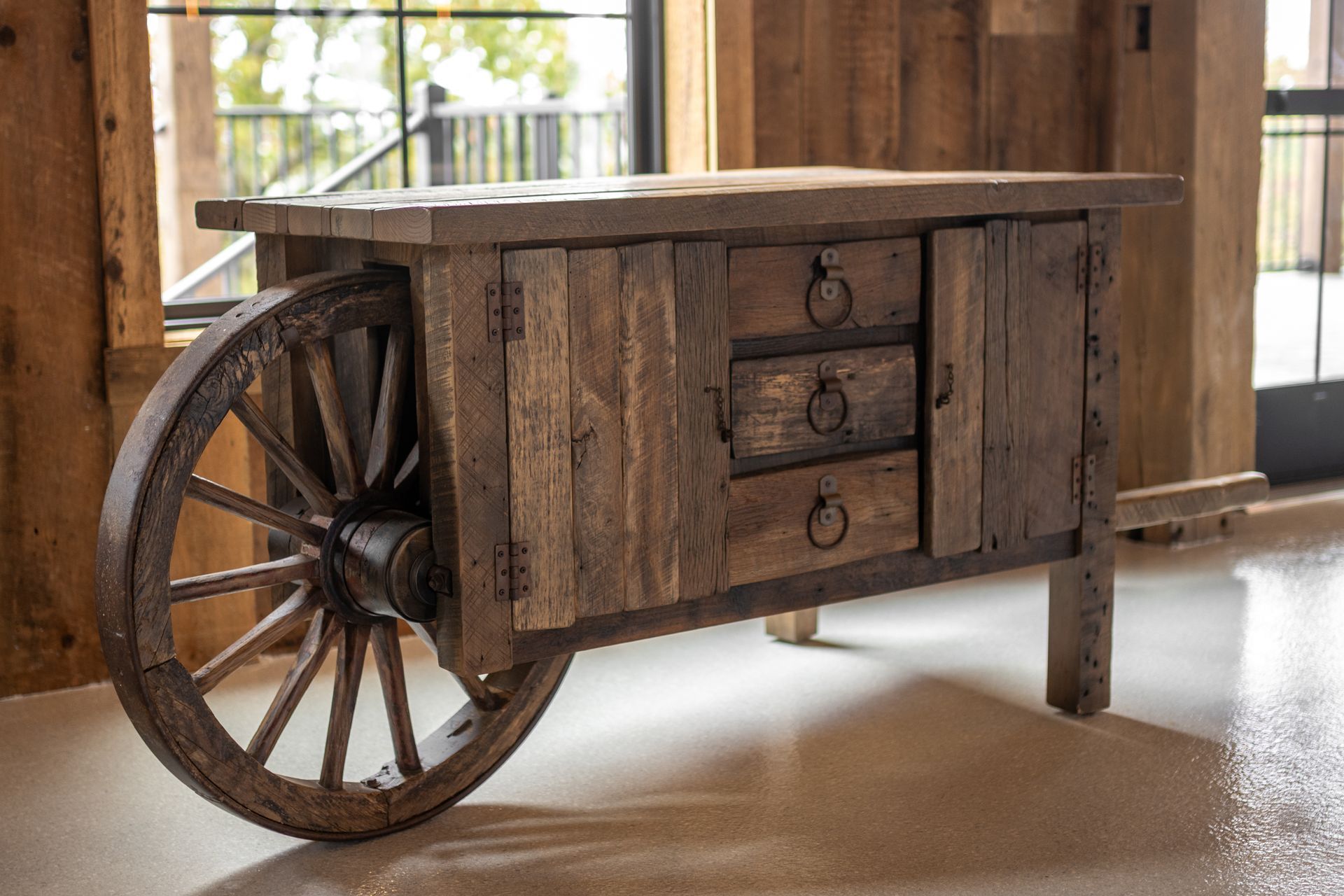 Rustic wooden cart with a large wheel, displayed indoors on a polished floor