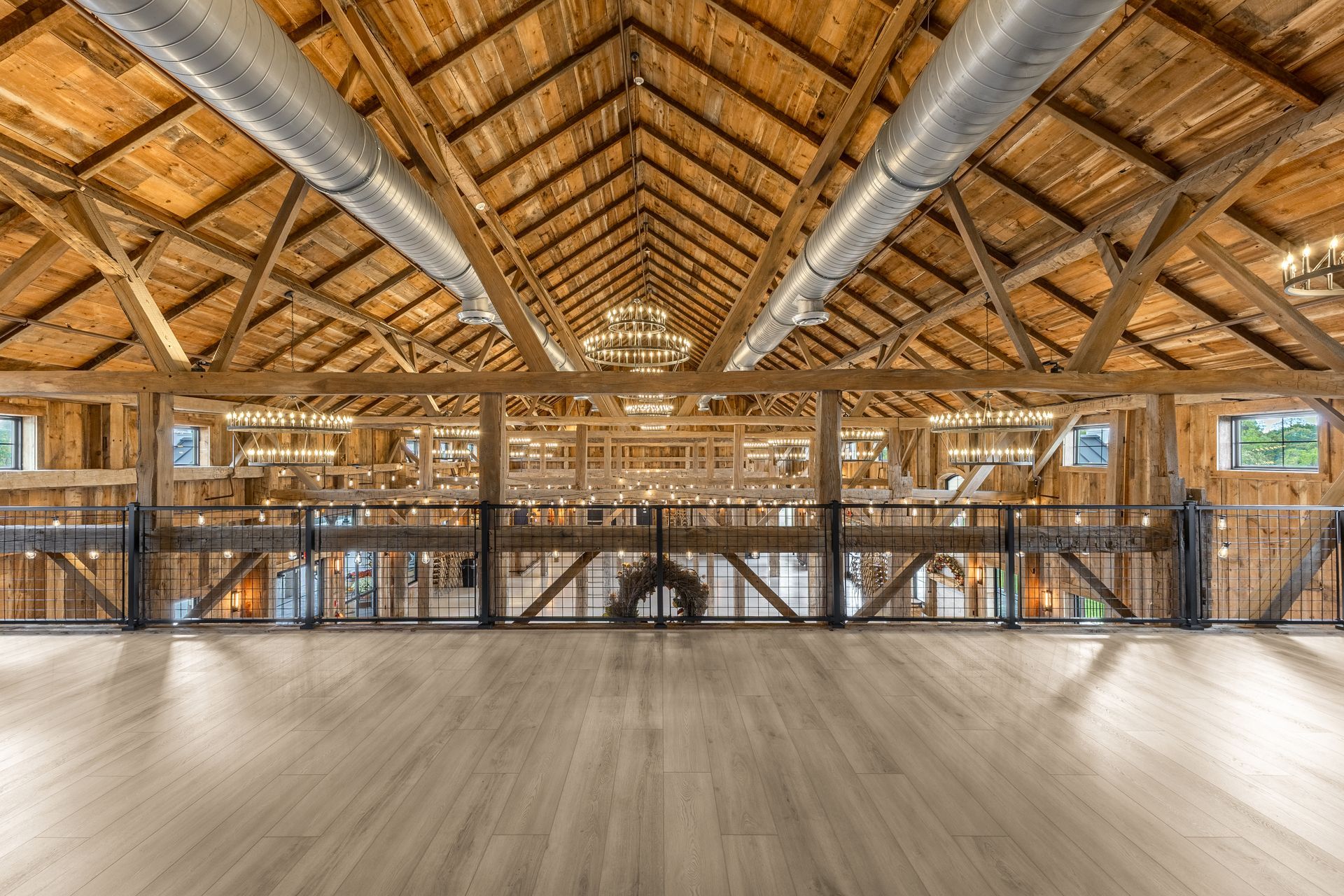Large open wooden hall with exposed beams, metal ducts, and wide empty floor overlooking a lower level