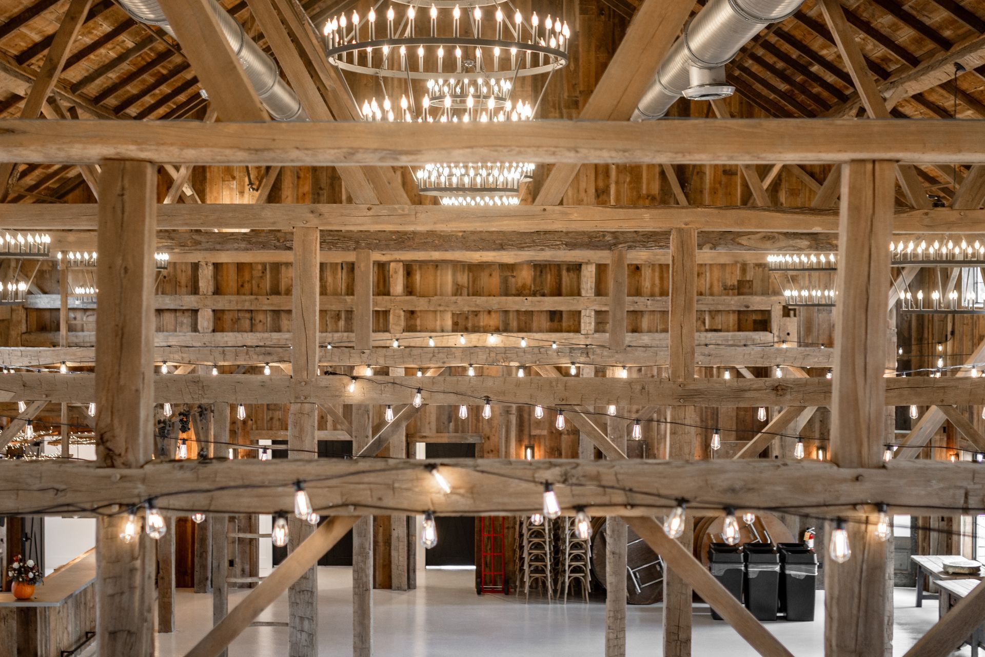 Interior of a large wooden barn with exposed beams and warm lighting, showing a spacious loft and open floor below