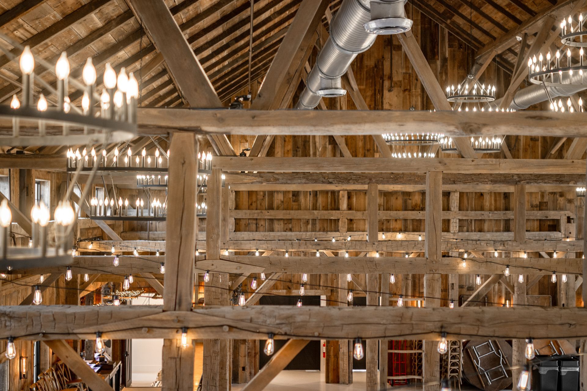 Industrial-style wooden interior with exposed beams, metal ducts, and glowing chandeliers
