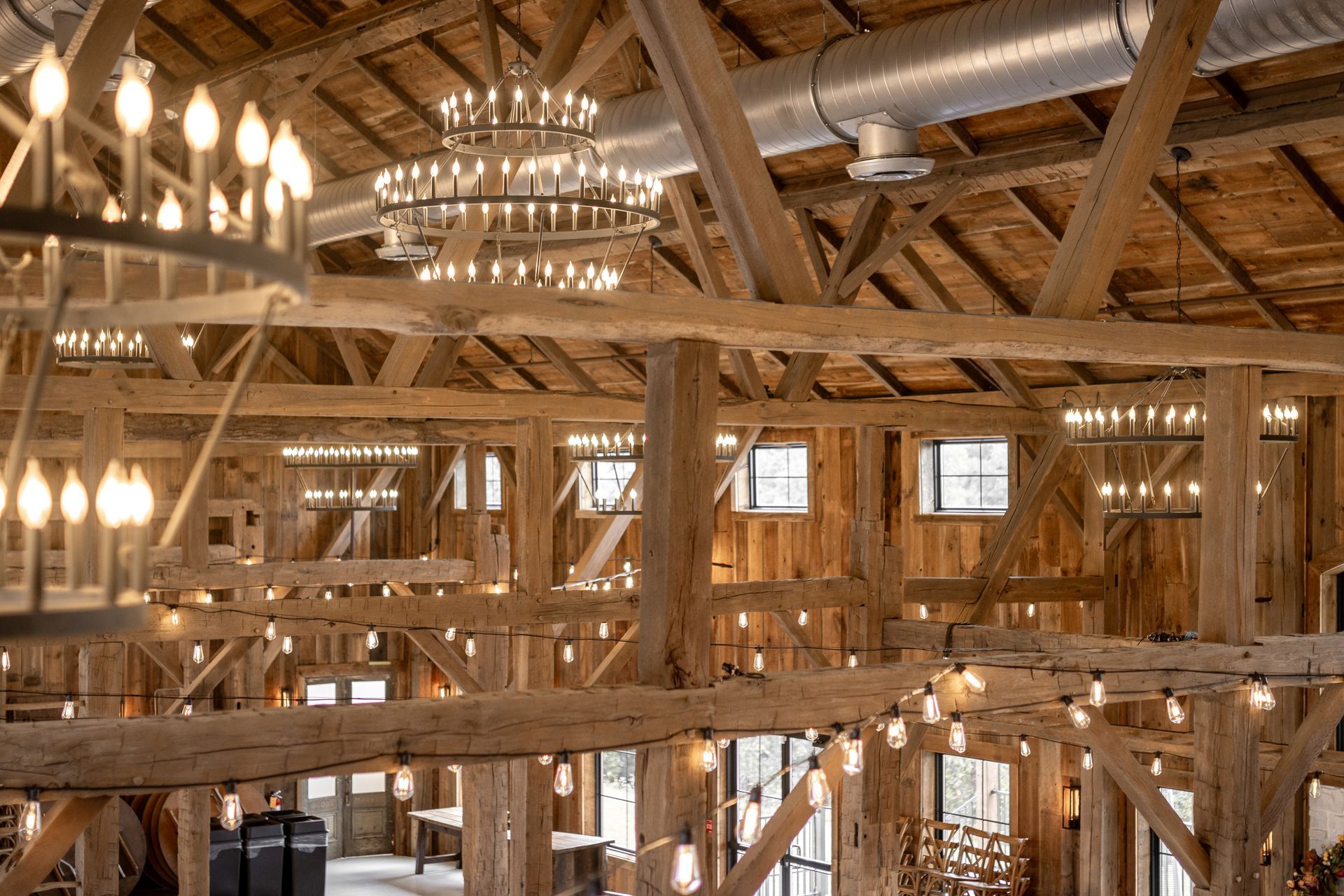 Rustic timber hall interior with exposed beams, chandeliers, and warm lighting